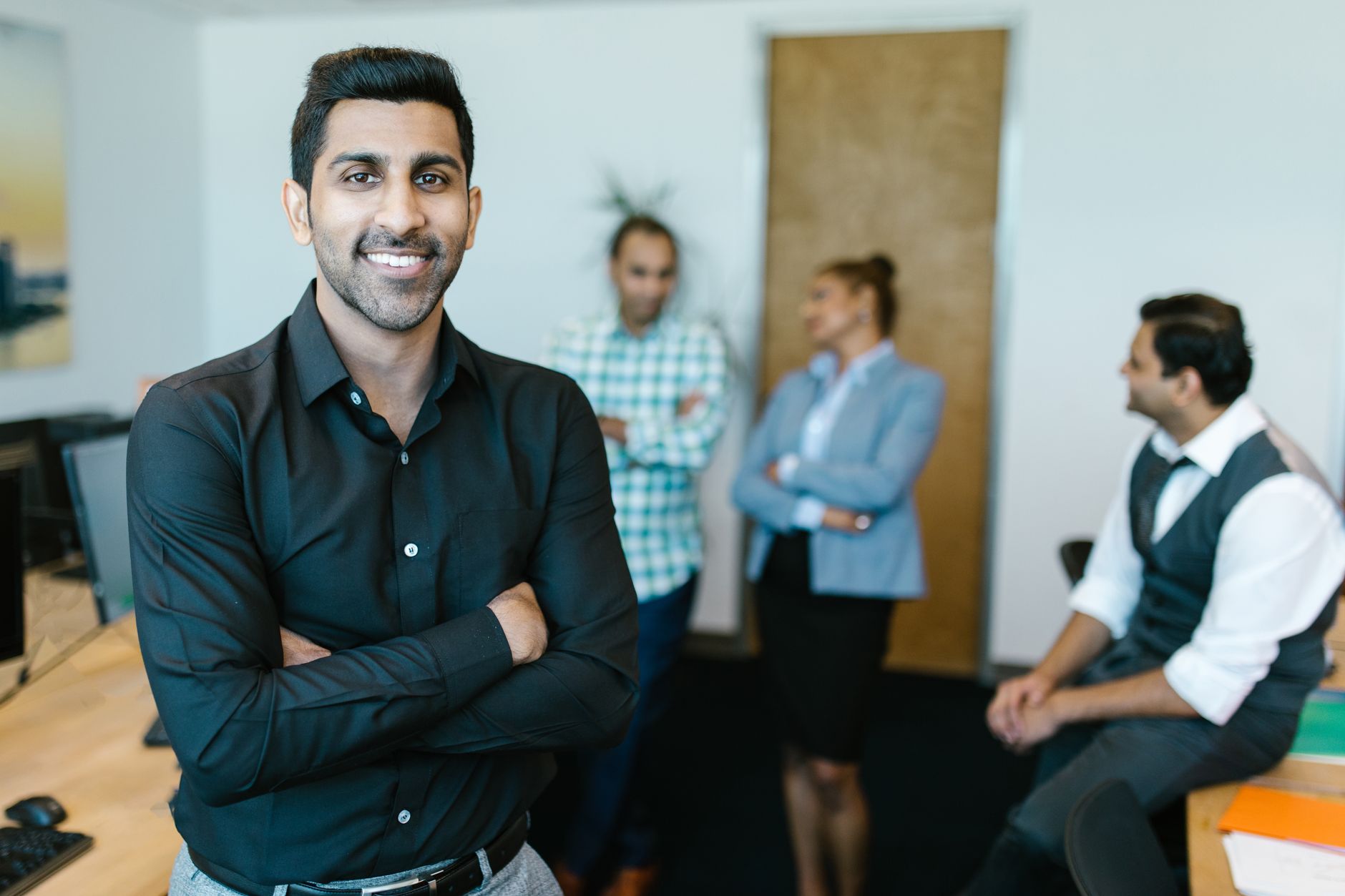 A confident young professional standing in a modern office with colleagues interacting in the background — UPI Study