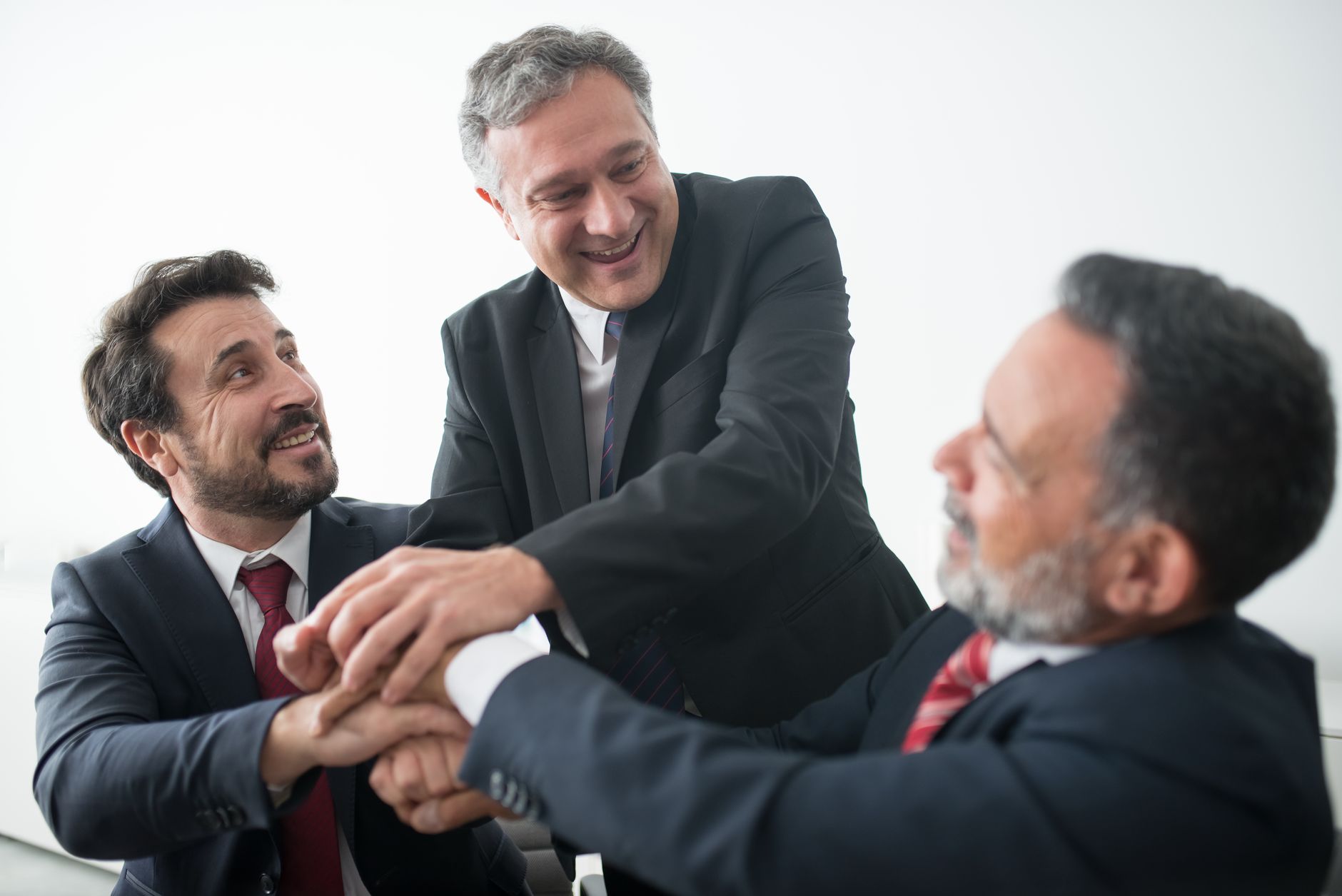 Three businessmen in suits celebrating teamwork success indoors with handshake — UPI Study