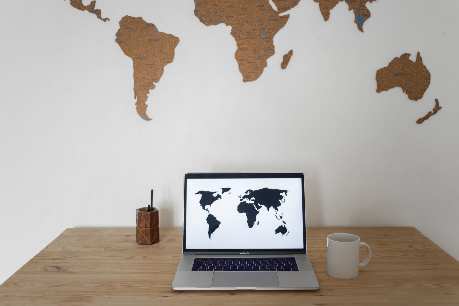 Black world map on laptop screen and ceramic cup with pen container placed on table against silhouettes of continents — UPI Study