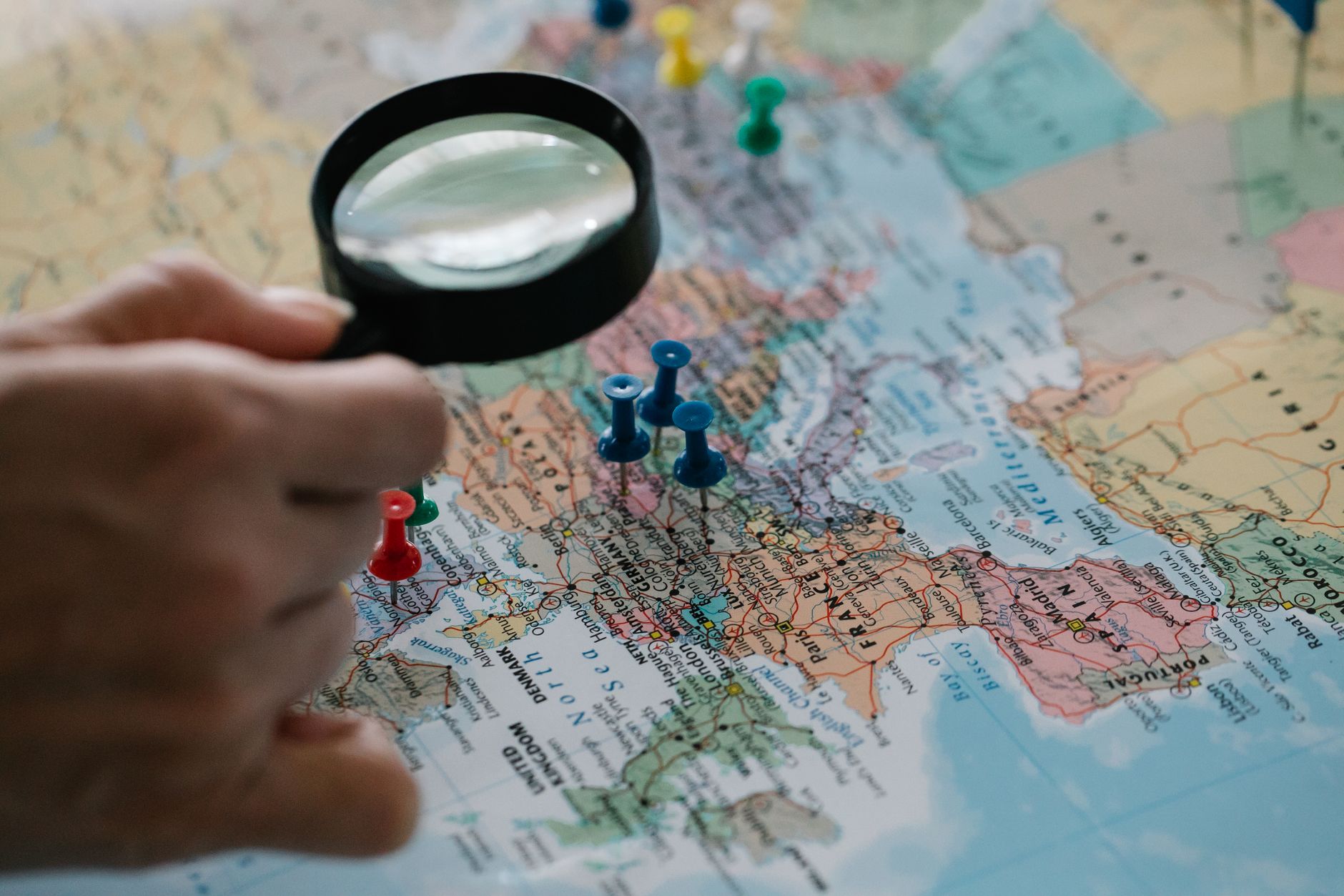 Magnifying glass focuses on pins highlighting travel destinations on a world map — UPI Study