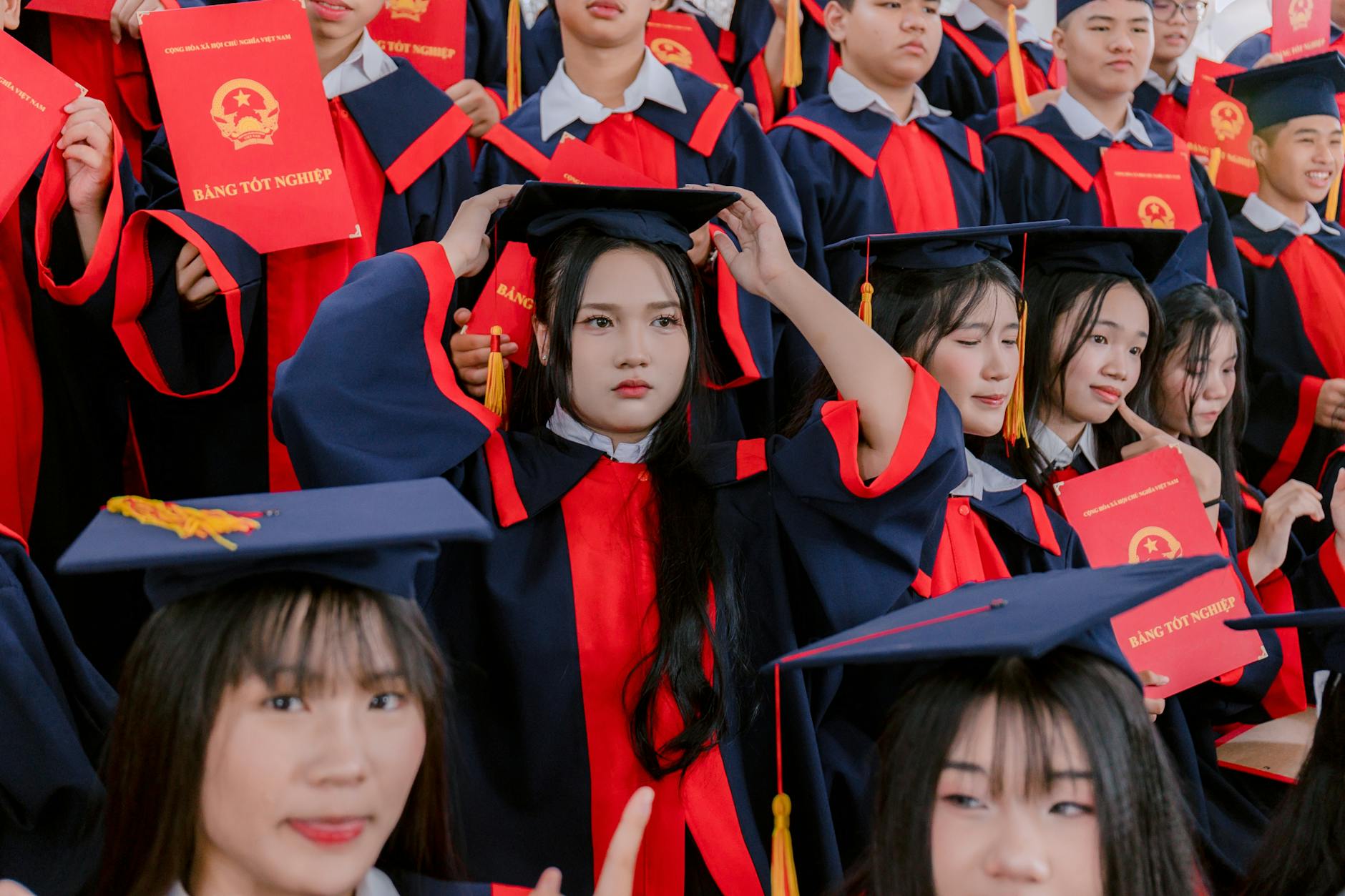 A large group of graduates in caps and gowns celebrate their ceremony, holding diplomas — UPI Study