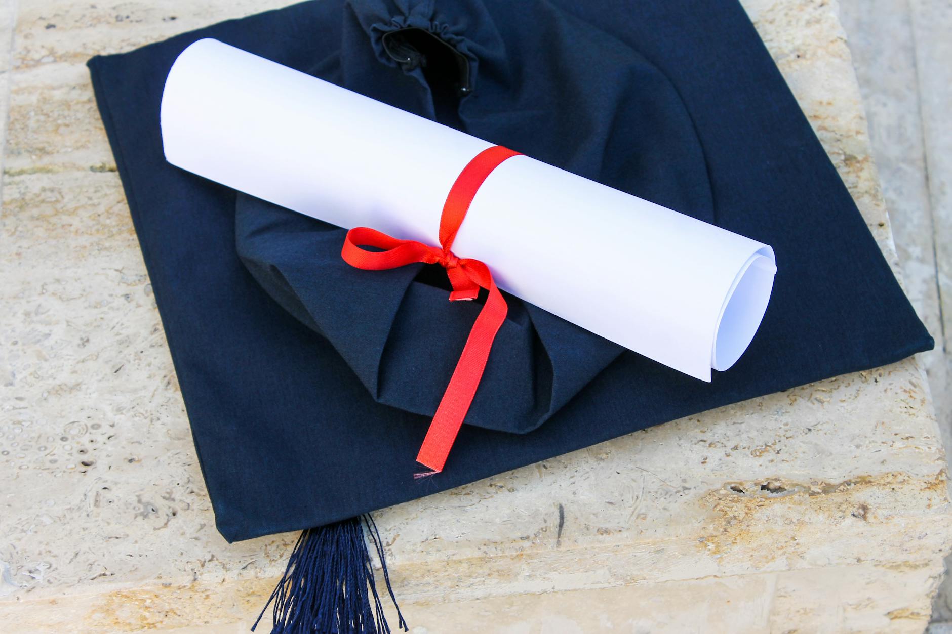 Graduation cap with diploma roll tied with red ribbon on concrete surface — UPI Study