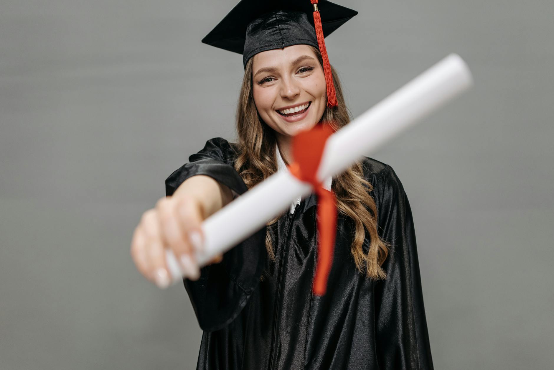 Happy female graduate wearing a cap and gown proudly holding her diploma with a smile — UPI Study