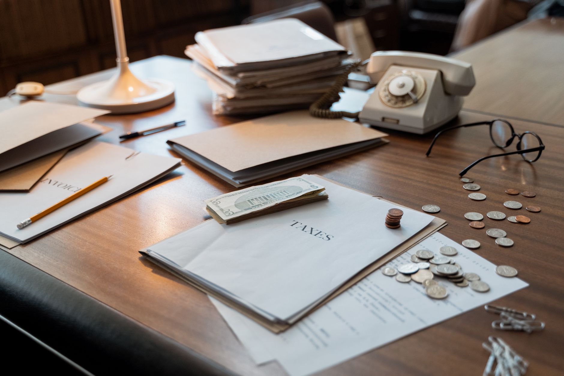Close-up of an office desk with tax documents, coins, glasses, and an old phone, symbolizing finance and organization — UPI Study