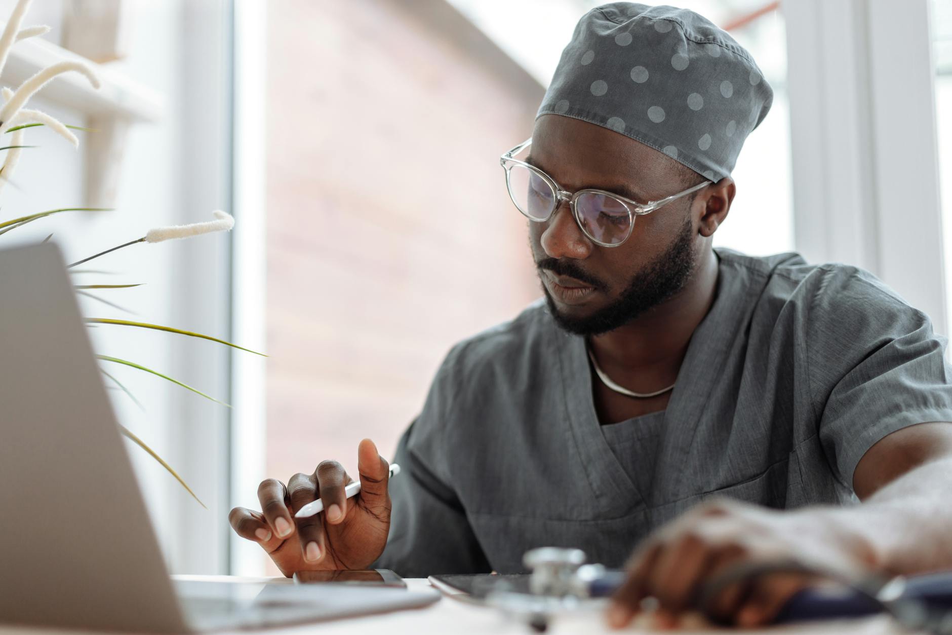 A focused male doctor in scrubs working on a laptop, showcasing professionalism and modern healthcare technology — UPI Study