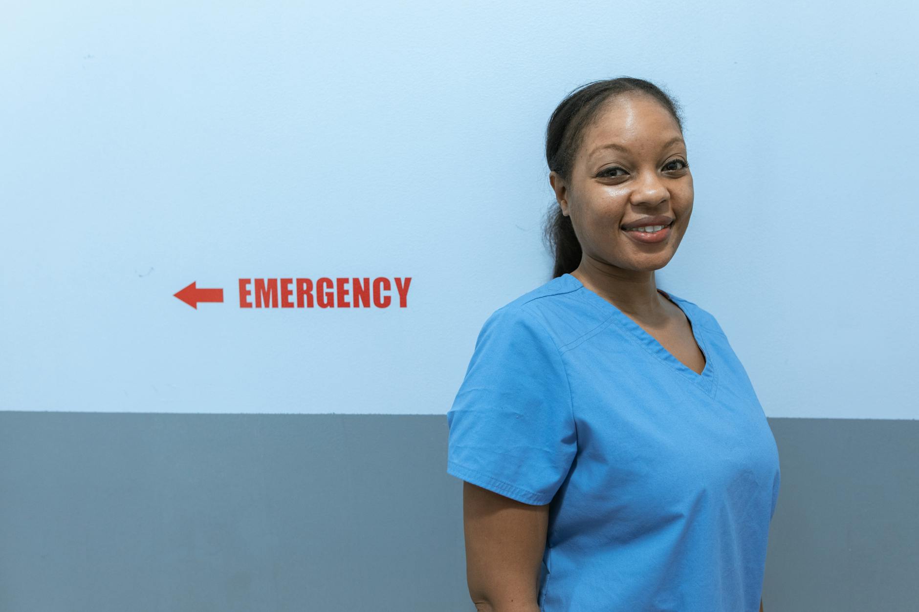 Happy healthcare worker in scrubs standing near emergency room sign — UPI Study