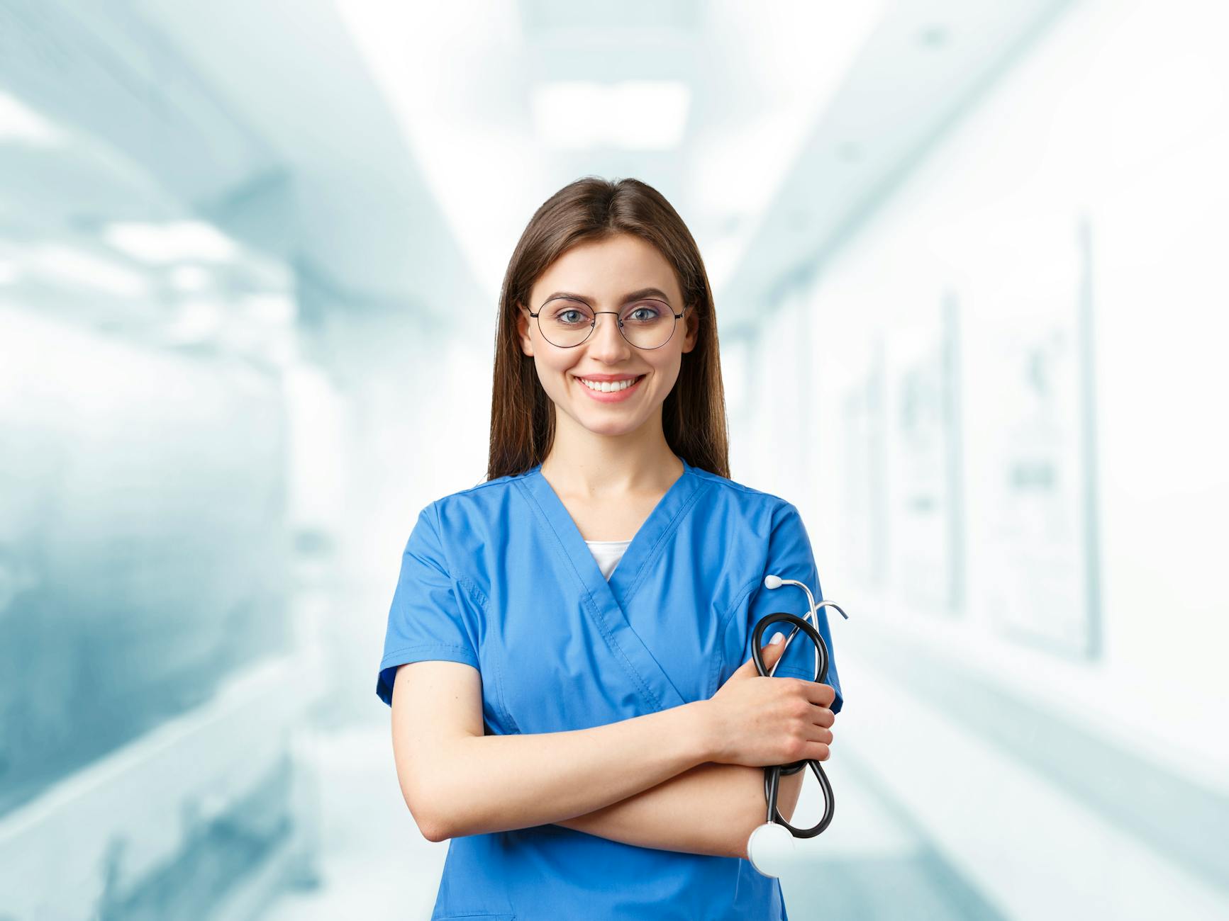 Young nurse in blue scrubs smiling and holding a stethoscope in a hospital corridor — UPI Study