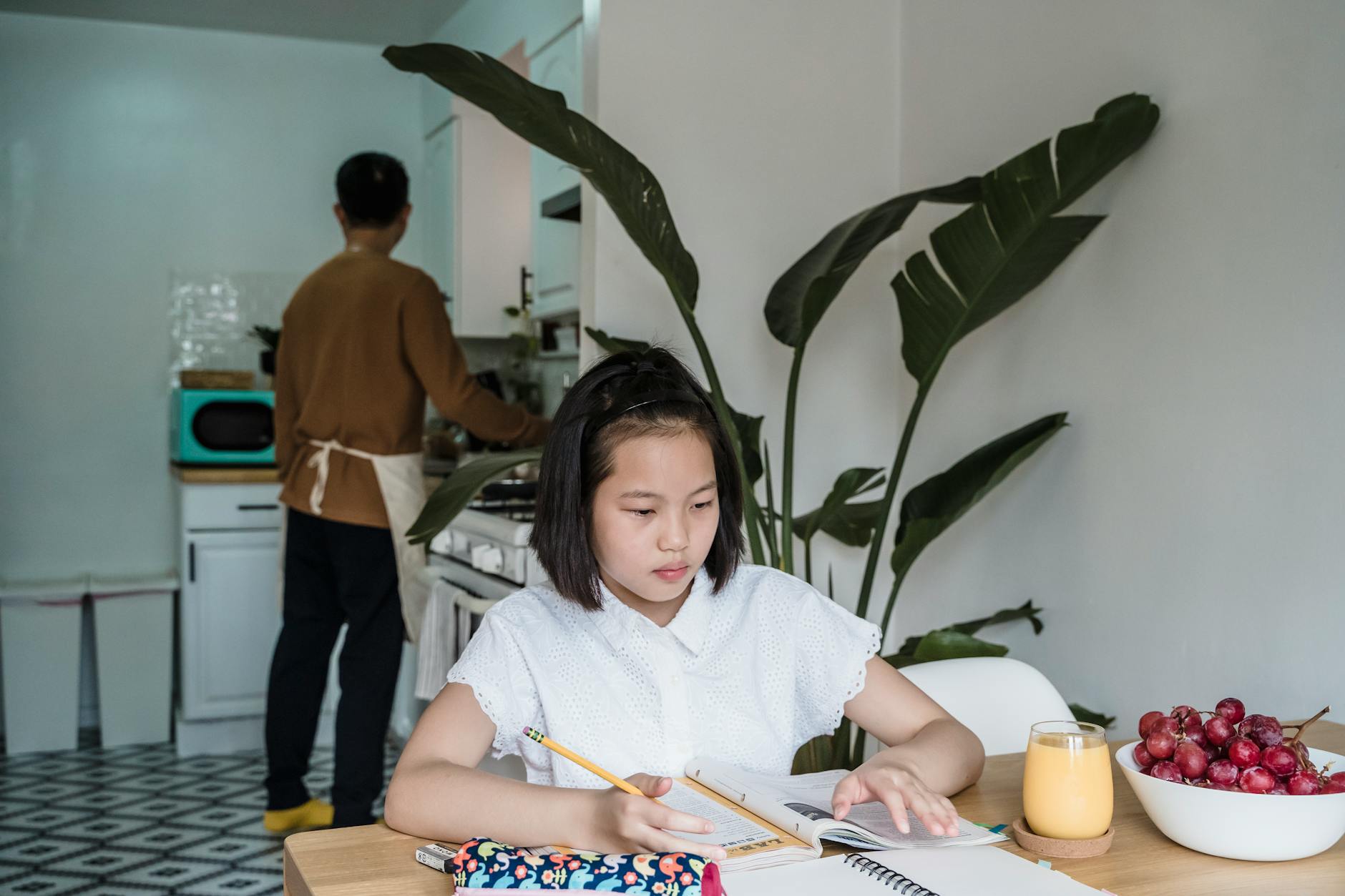 Girl focuses on homework at the kitchen table with fruit and juice nearby — UPI Study