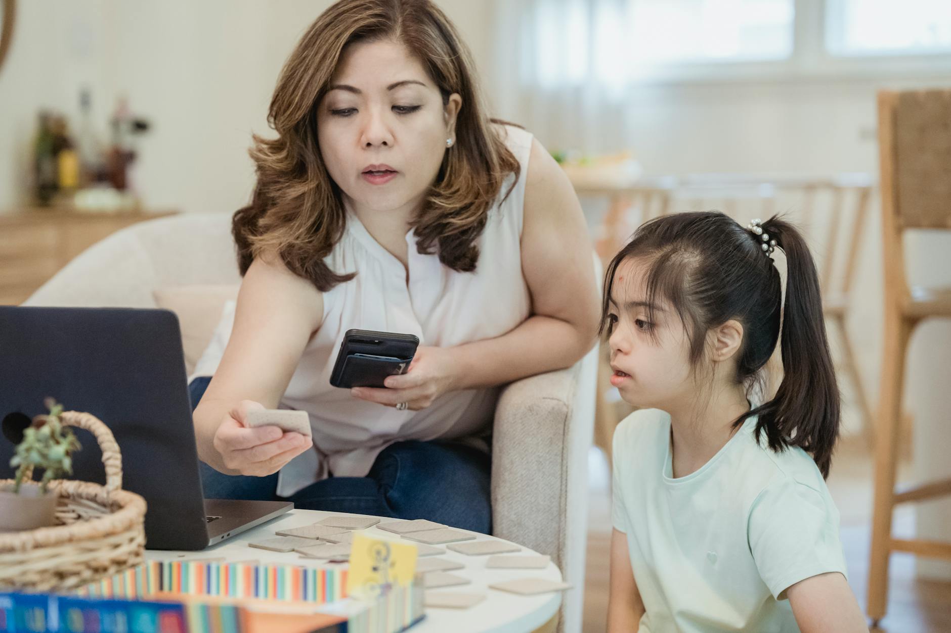 A mother guides her daughter in learning activities using cards and a laptop at home — UPI Study