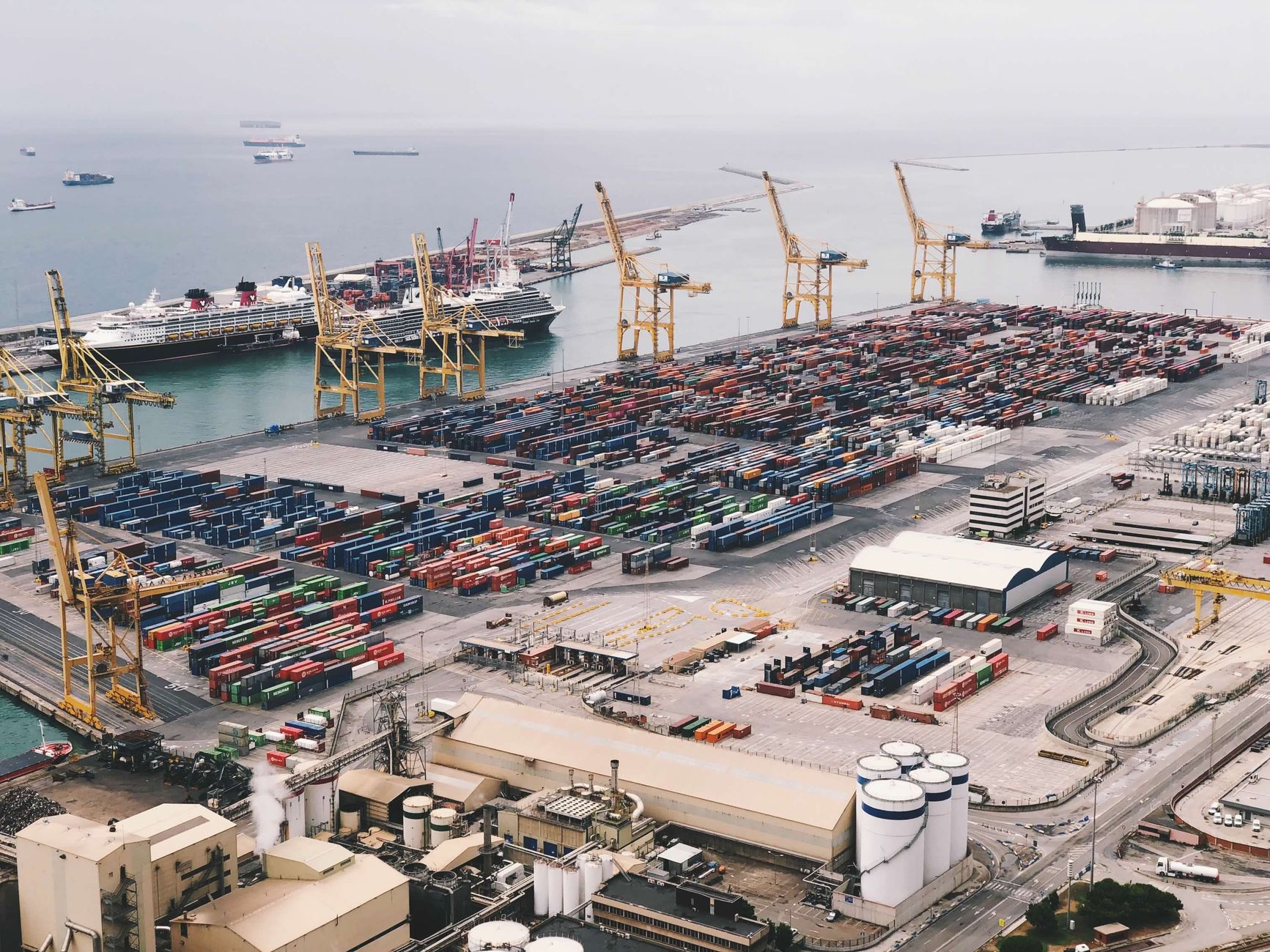 Expansive aerial view of a bustling container port with large cranes and cargo ships under a cloudy sky — UPI Study