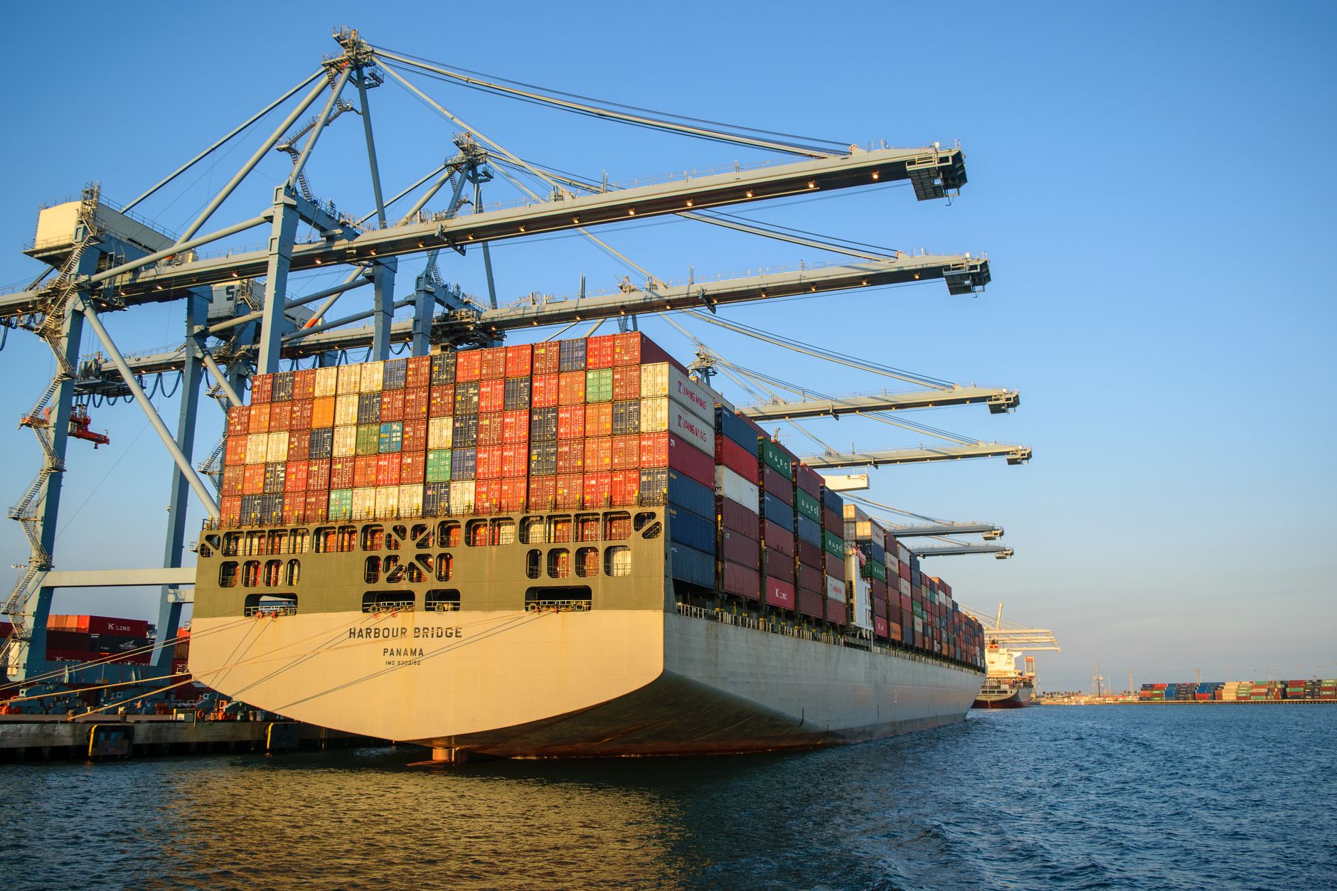 A large container ship at an industrial harbor with cranes under a clear blue sky — UPI Study