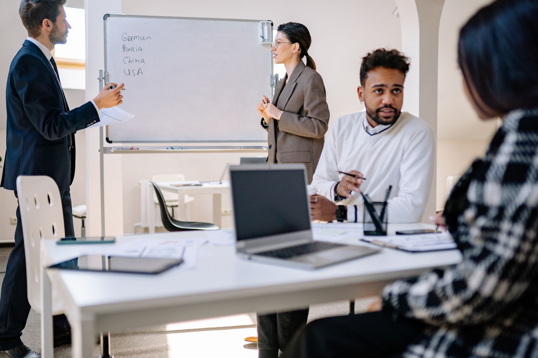 A diverse group of professionals engaged in a collaborative office meeting with laptops and a whiteboard — UPI Study