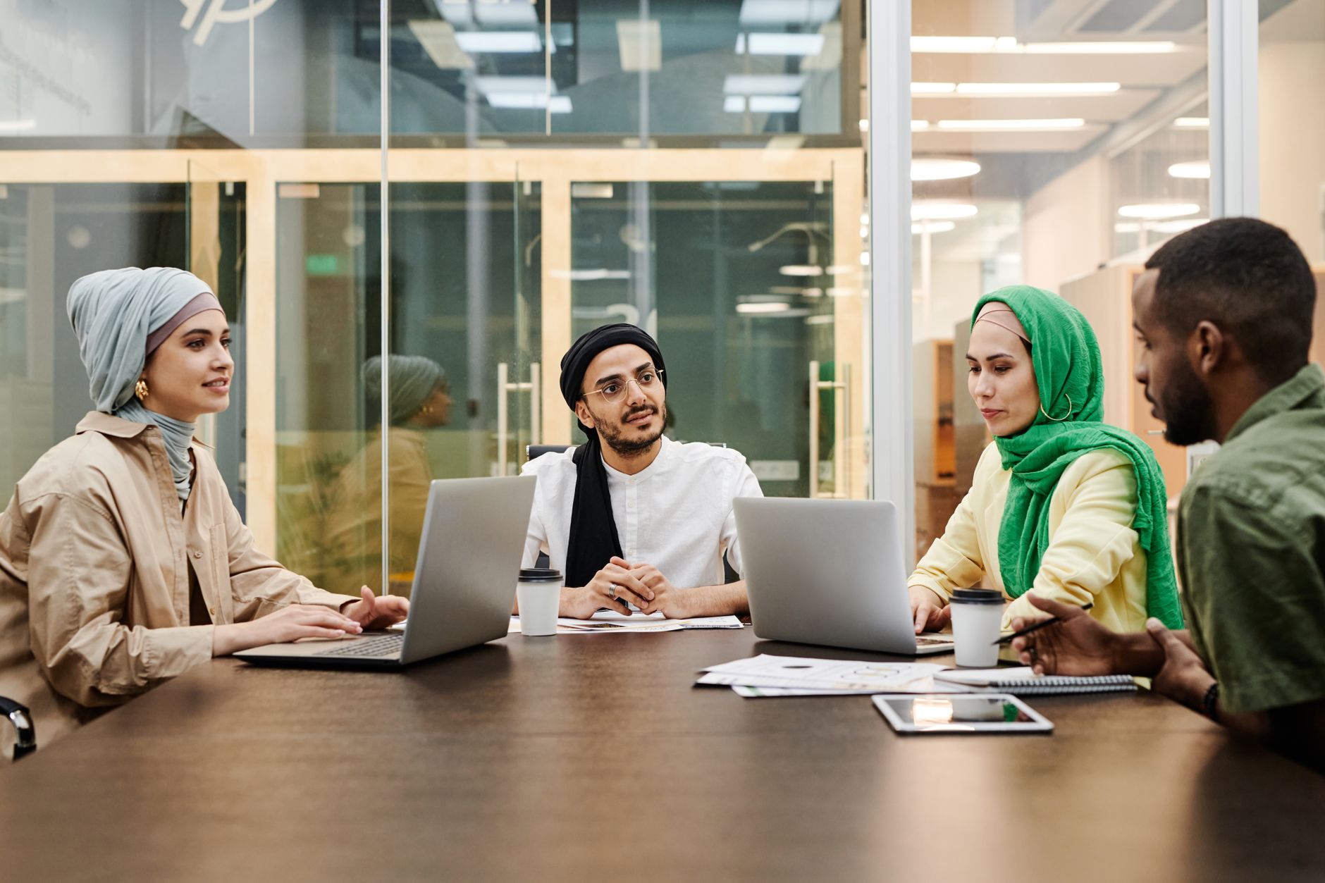 A diverse group discussing ideas in a modern office setting, using laptops and tablets — UPI Study