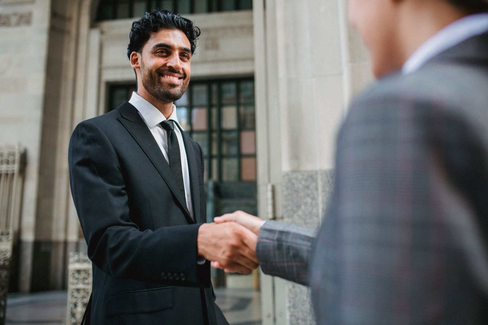 Two business professionals shake hands confidently in an urban setting — UPI Study