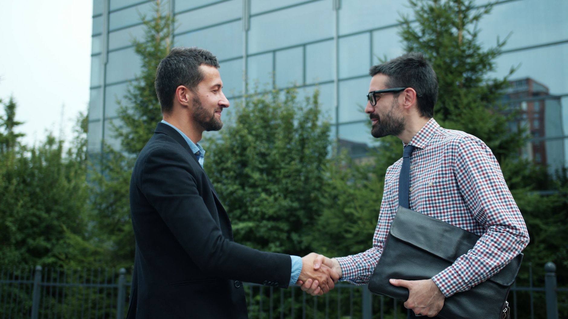 Two businessmen shaking hands outside an office building, symbolizing partnership — UPI Study