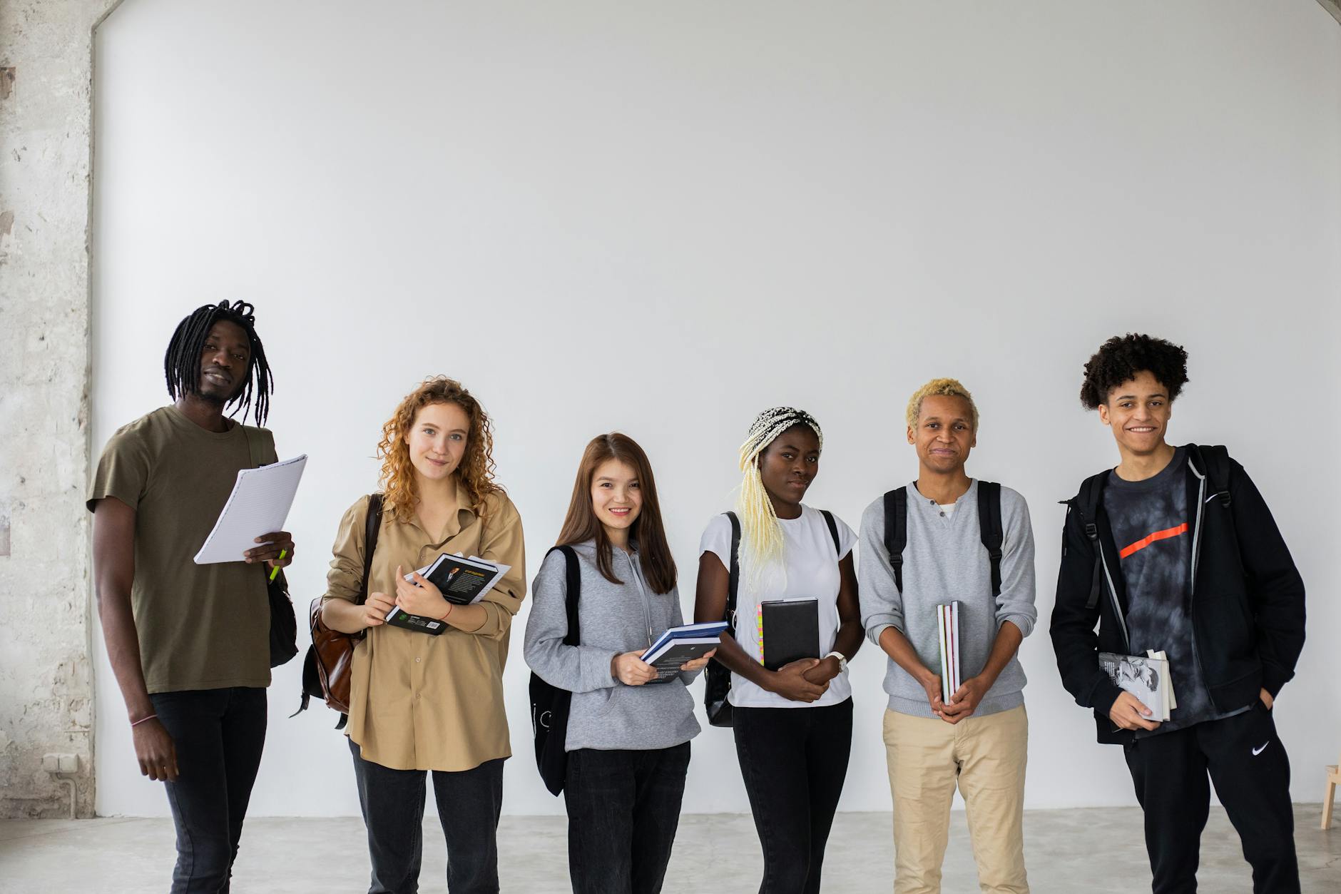 Group of diverse young multiracial classmates with notebooks and textbooks and backpacks smiling at camera — UPI Study