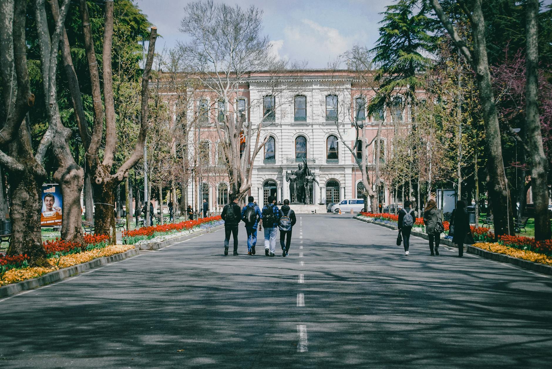 Students walking on a university campus surrounded by trees and spring flowers — UPI Study