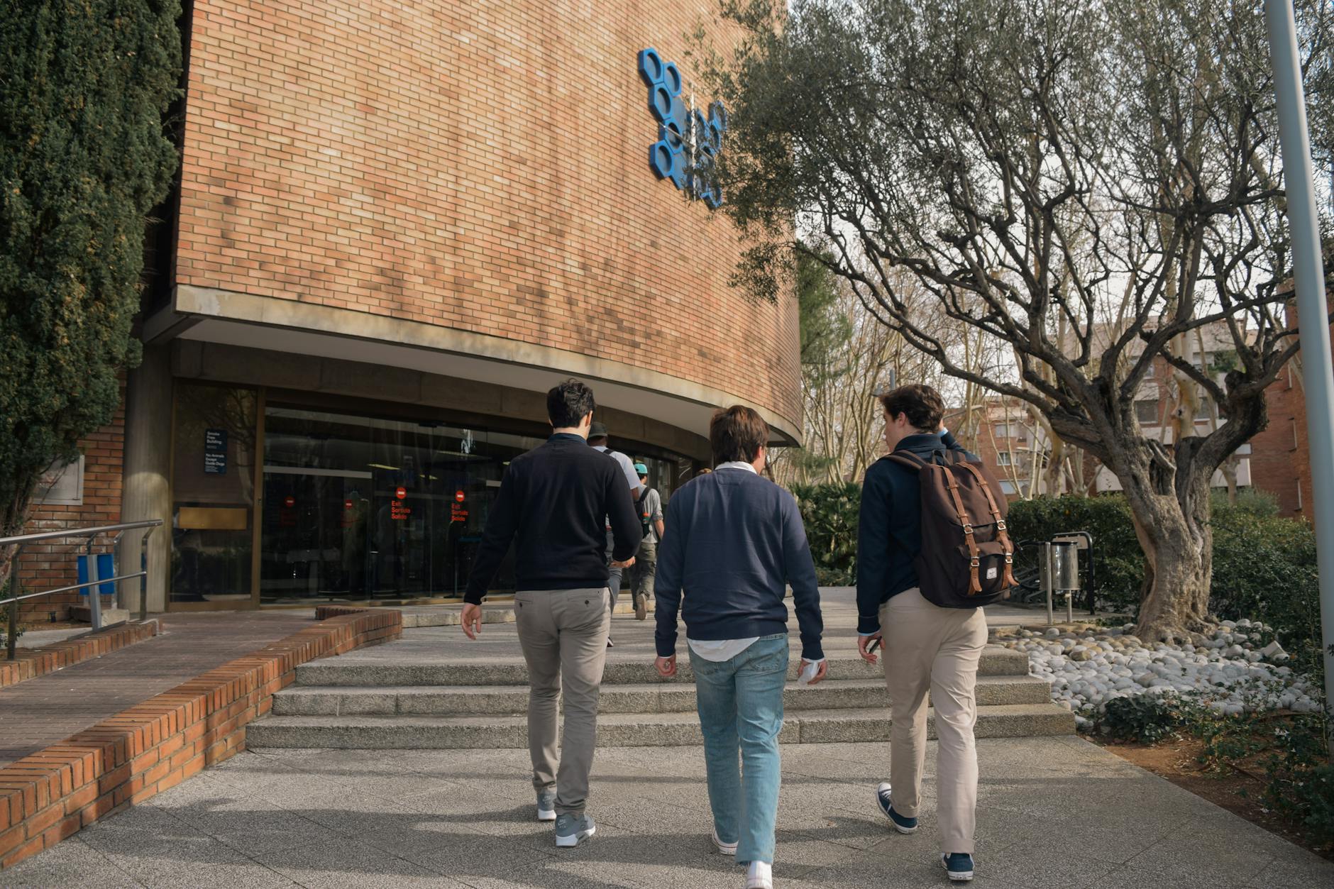 Three students approach a university building entrance in Barcelona, Spain on a sunny day — UPI Study