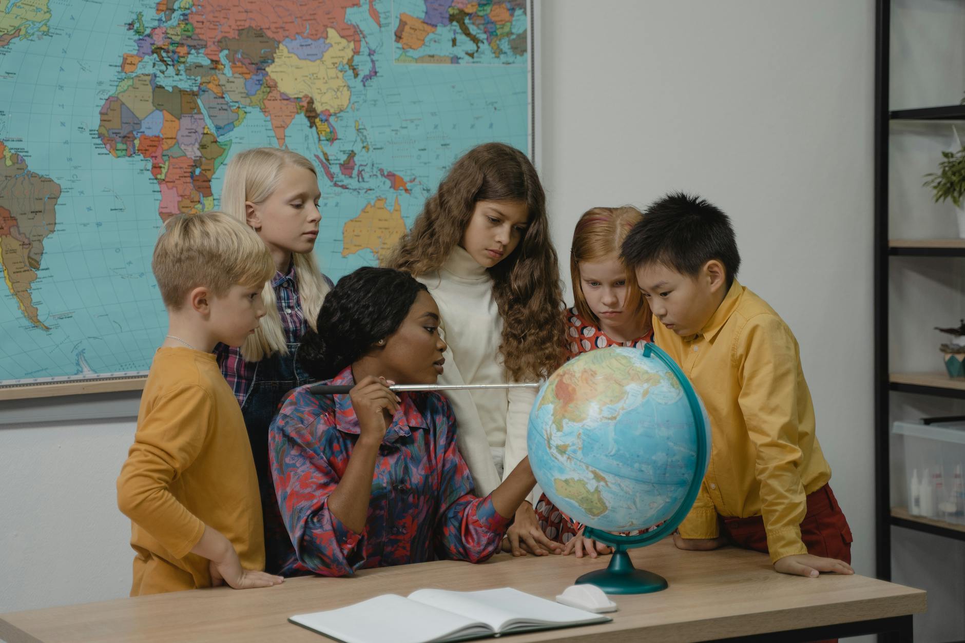 A diverse group of children learning geography with a teacher and globe in a classroom — UPI Study