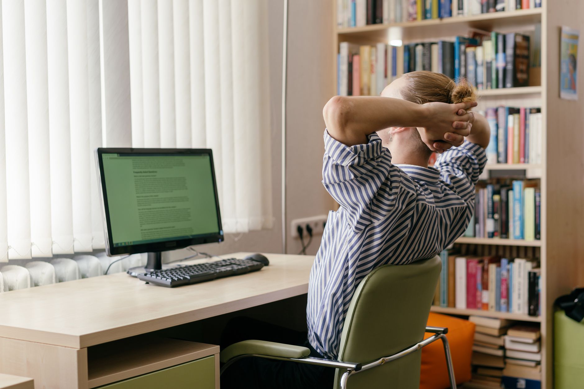 A young adult sits at a desk, hands on head, in a study space with a computer and bookshelves — UPI Study