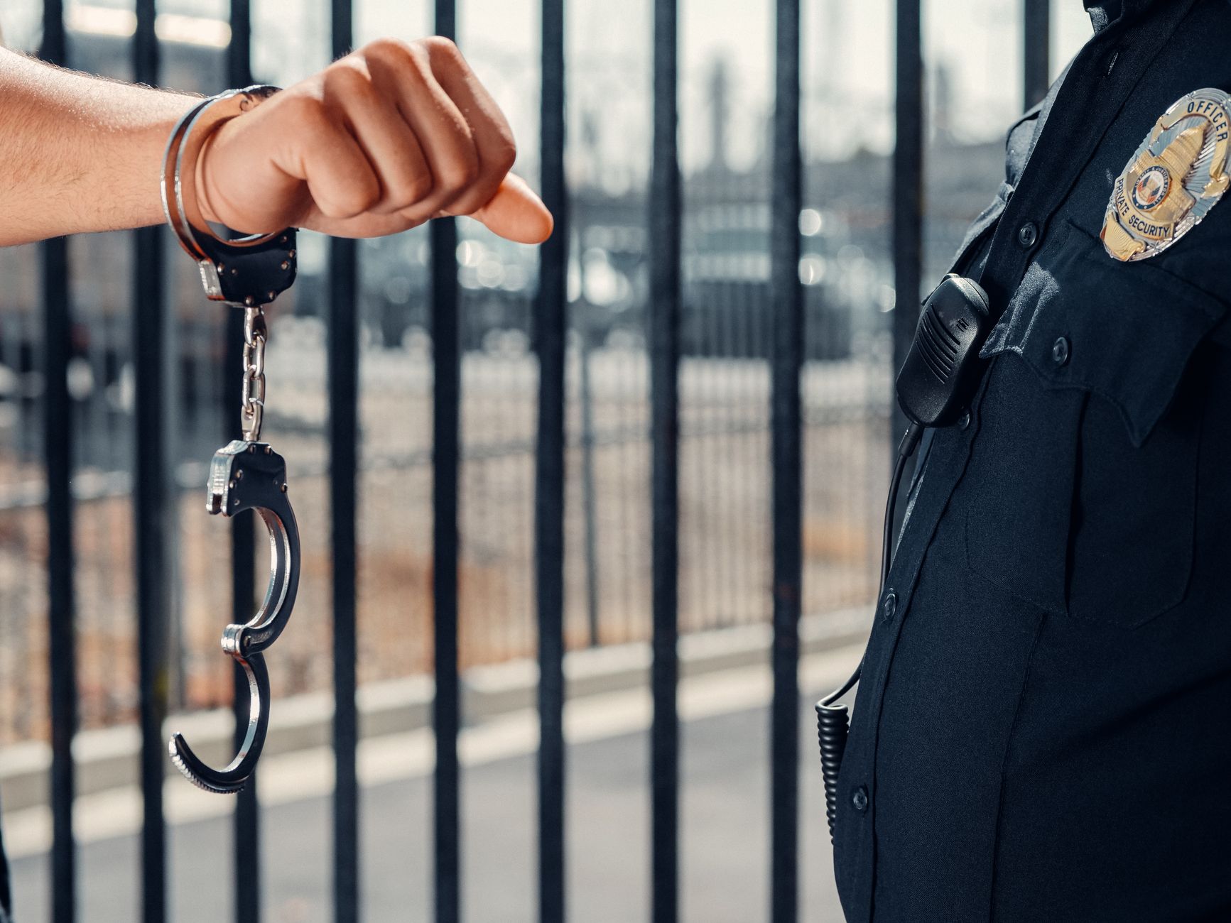Close-up of a police officer handcuffing an individual against a metal fence outdoors — UPI Study