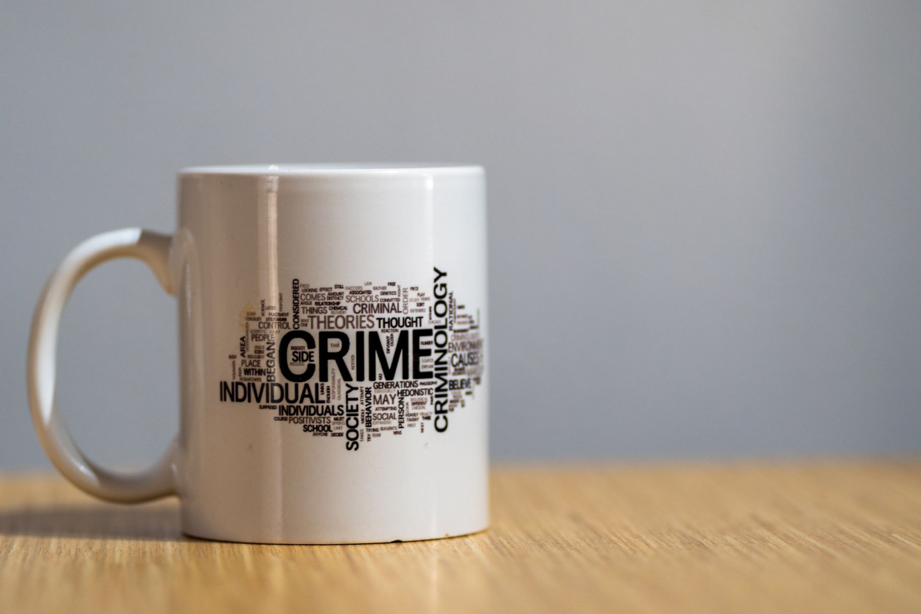 White ceramic mug with criminology-themed word cloud design on wooden surface — UPI Study