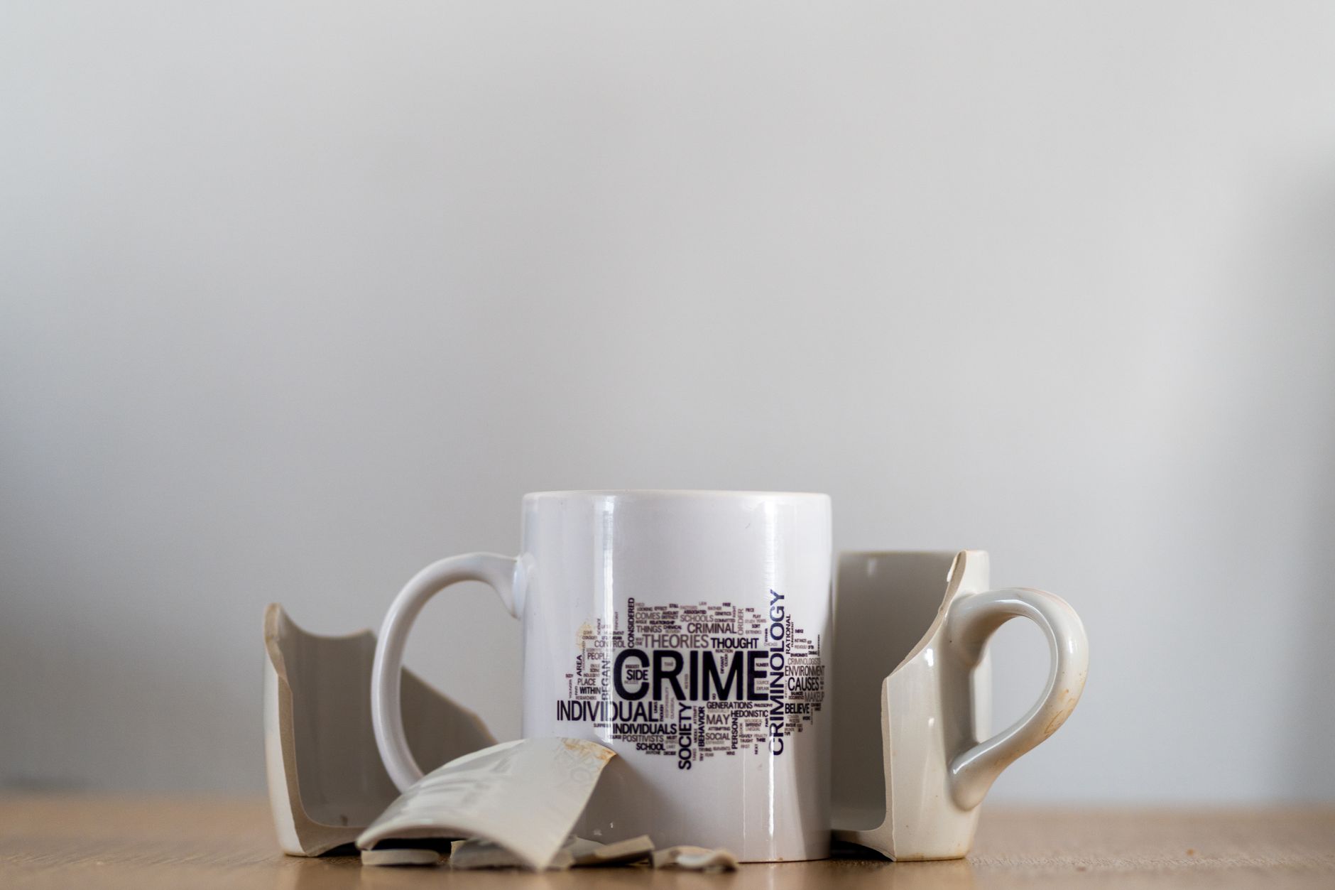 Artistic photo of a broken coffee cup featuring crime-related word art — UPI Study
