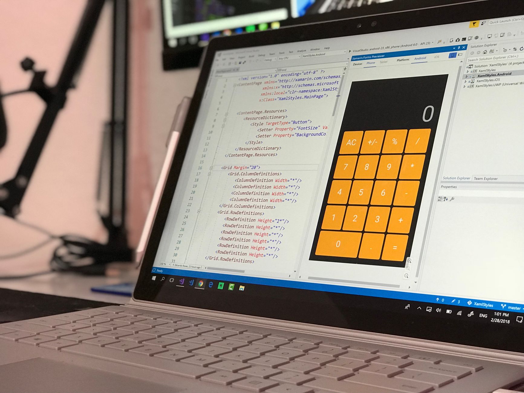 A laptop screen shows a coding application with a calculator design in a tech office setting — UPI Study