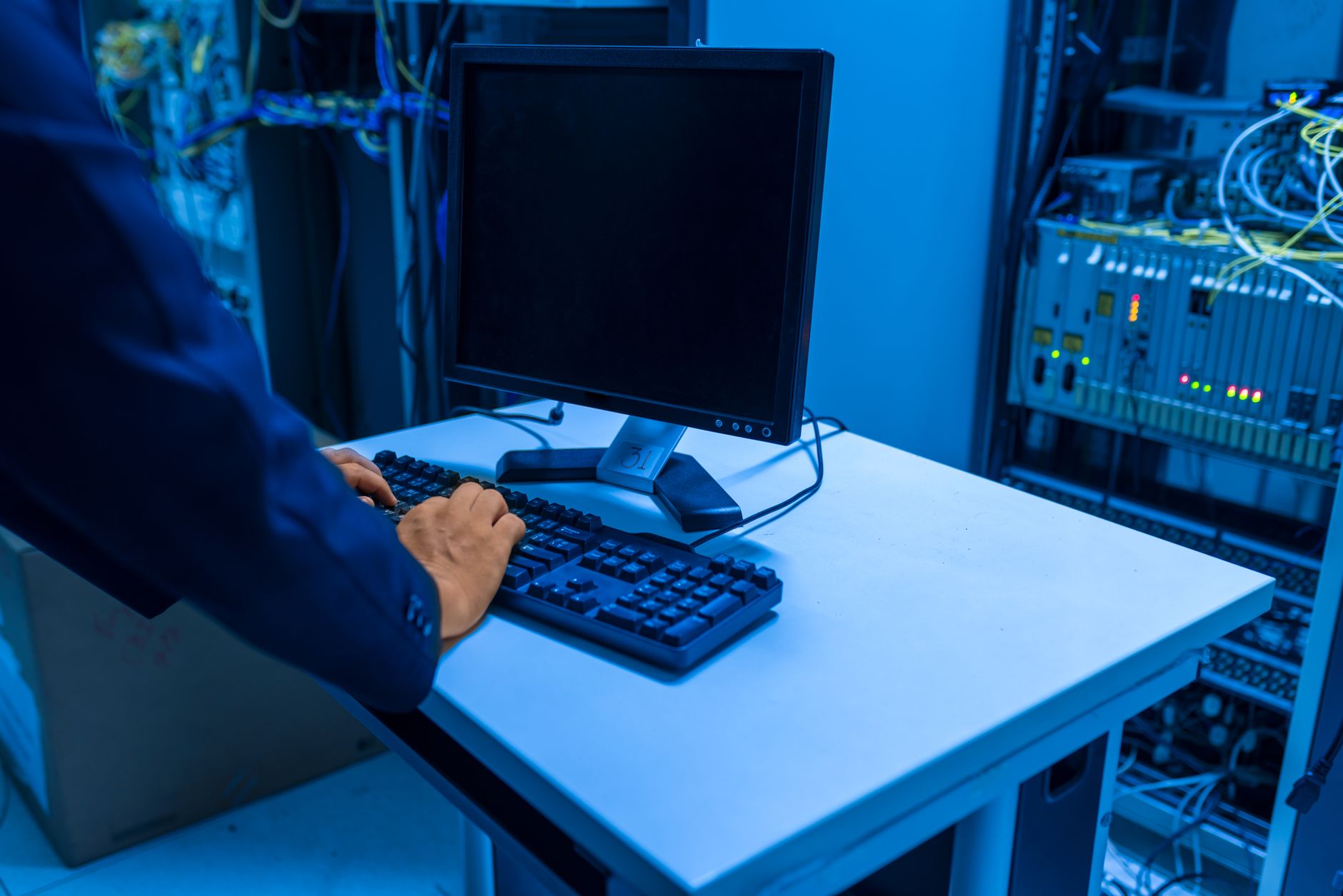 An IT professional operates a computer in a server room, managing network systems and connected devices — UPI Study