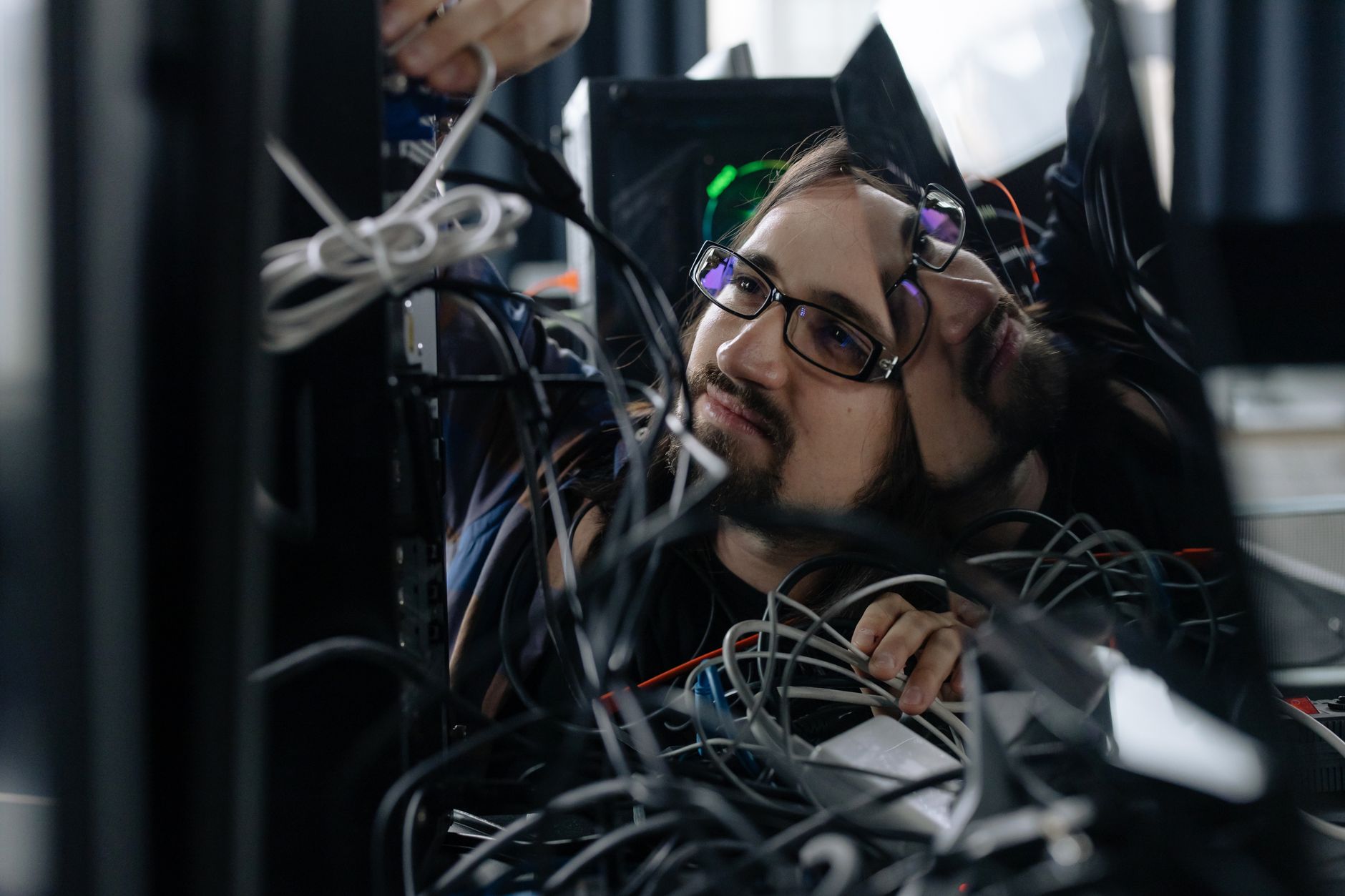 A skilled IT technician organizing tangled cables at his workstation in an office environment — UPI Study