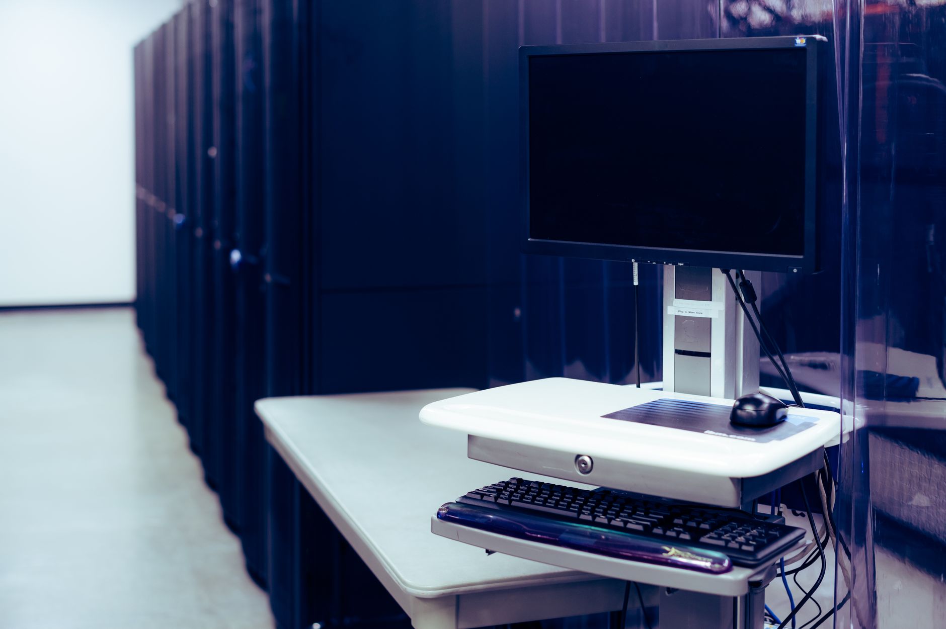 Contemporary computer with black screen placed on stand near row of server steel racks in data center — UPI Study