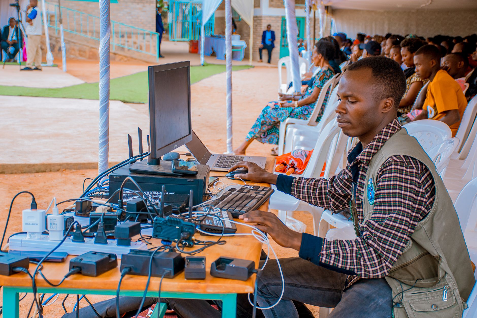 Technician managing electrical and computer setup at an outdoor event with attentive audience — UPI Study
