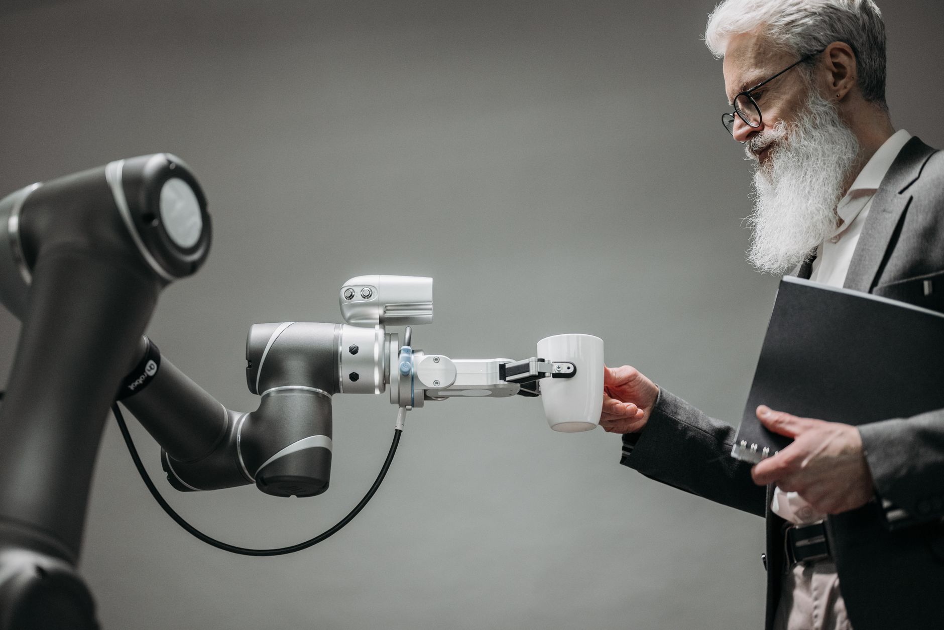 An elderly man receives a cup from a robotic arm in a modern office setting — UPI Study