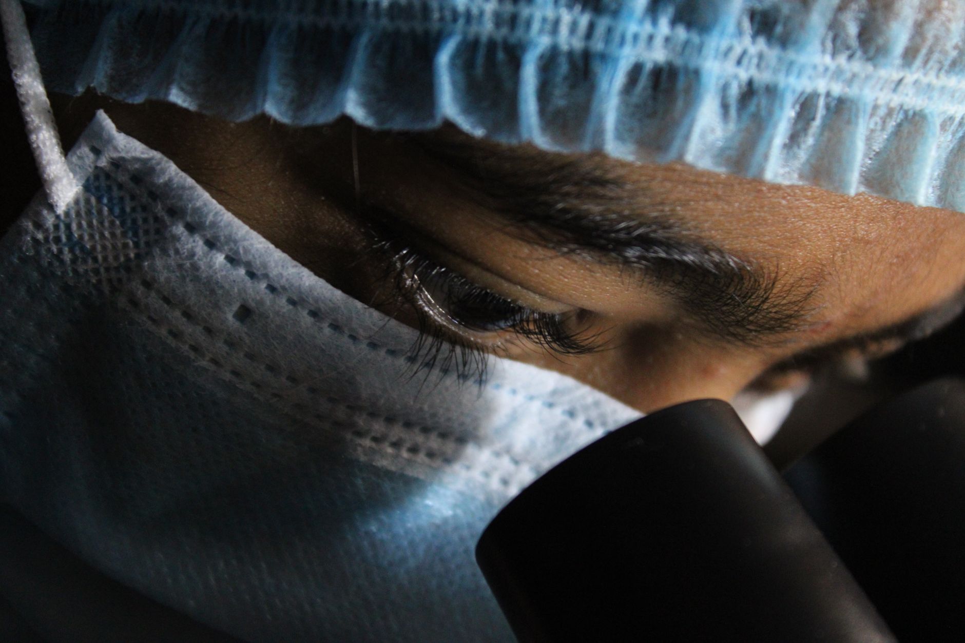 A scientist in protective gear intensely looking through a microscope — UPI Study