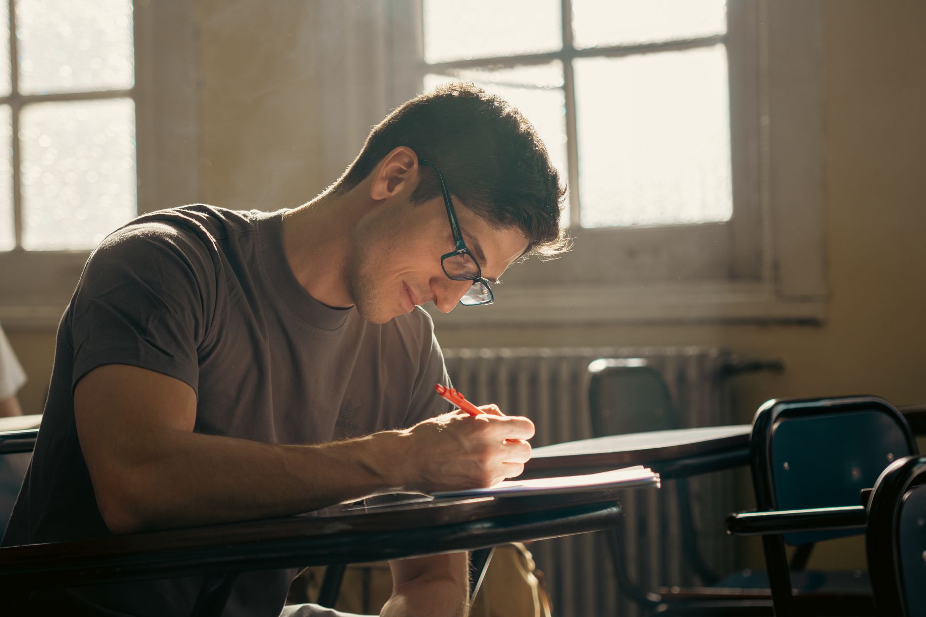 A student concentrating on writing during a class session in a warmly lit university classroom — UPI Study
