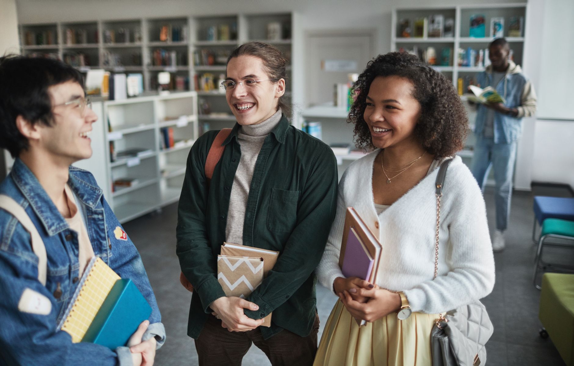 Group of diverse students laughing and holding books in a library environment — UPI Study