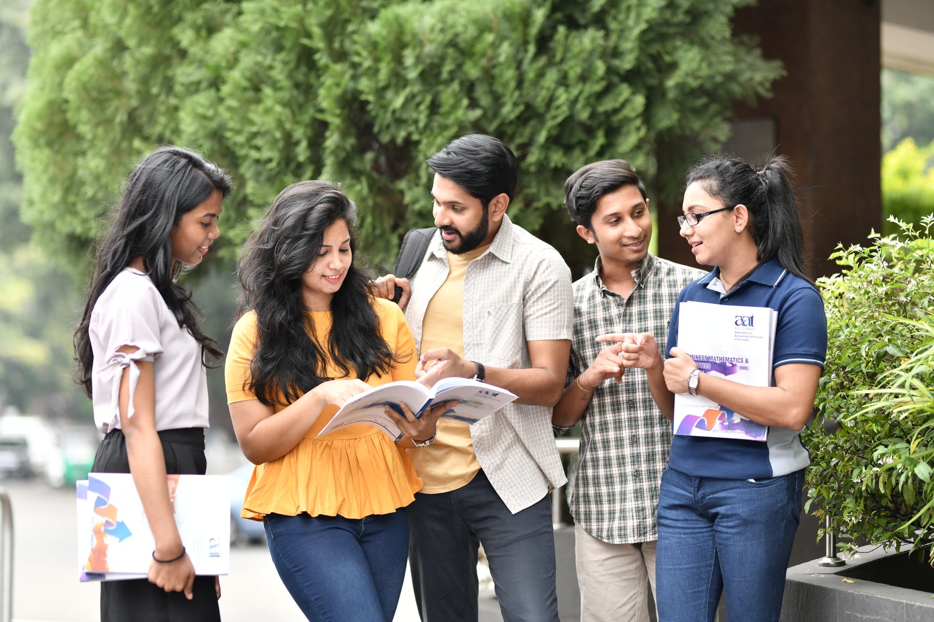 A group of diverse college students engaged in outdoor group study session, sharing books and ideas — UPI Study