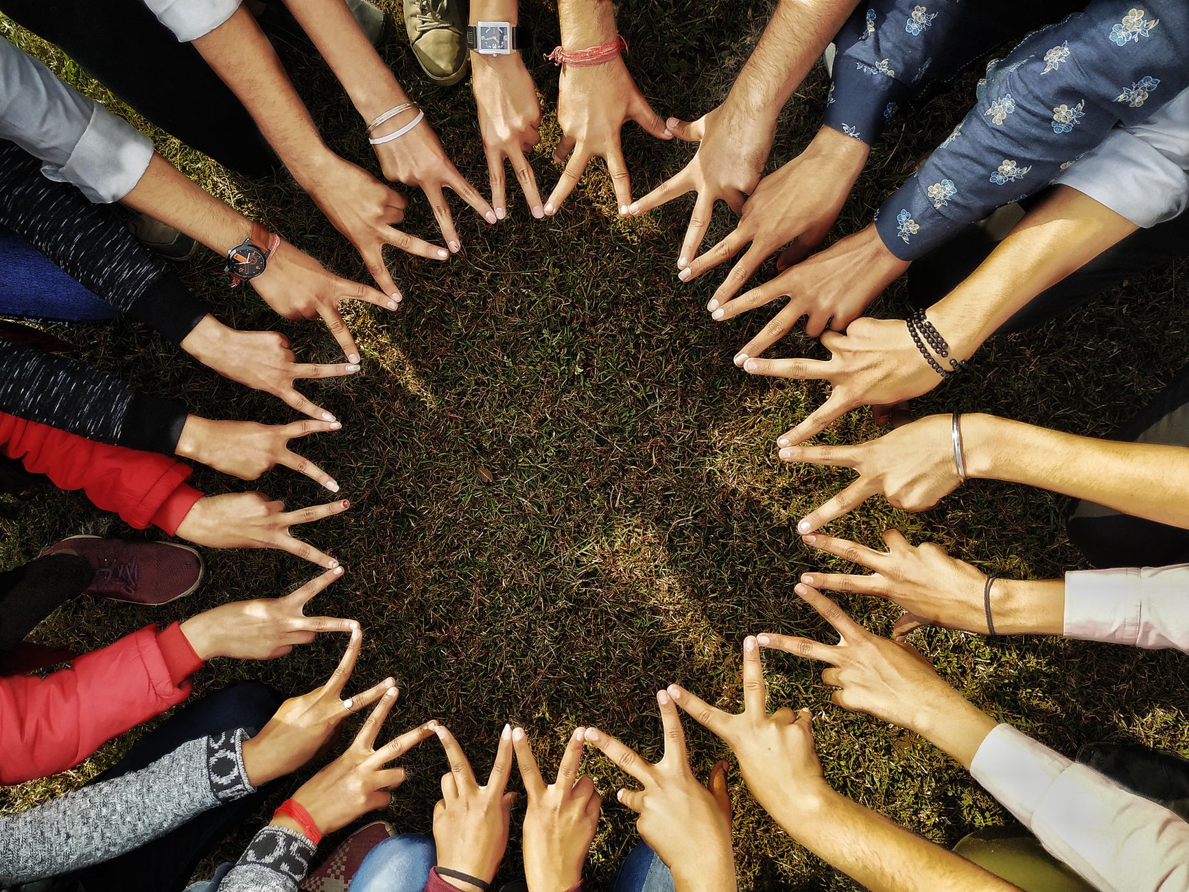 A diverse group of hands forming a star shape in a circle on grassy ground, symbolizing unity — UPI Study