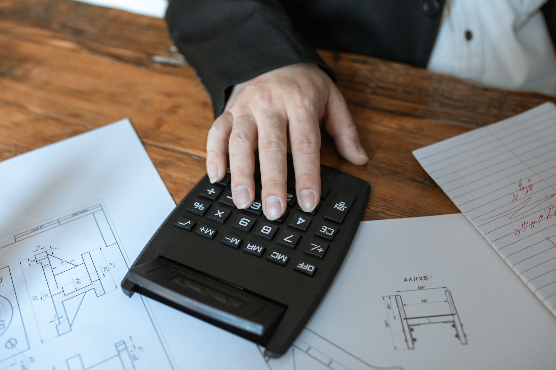 Hand using calculator for architectural calculations on blueprints — UPI Study