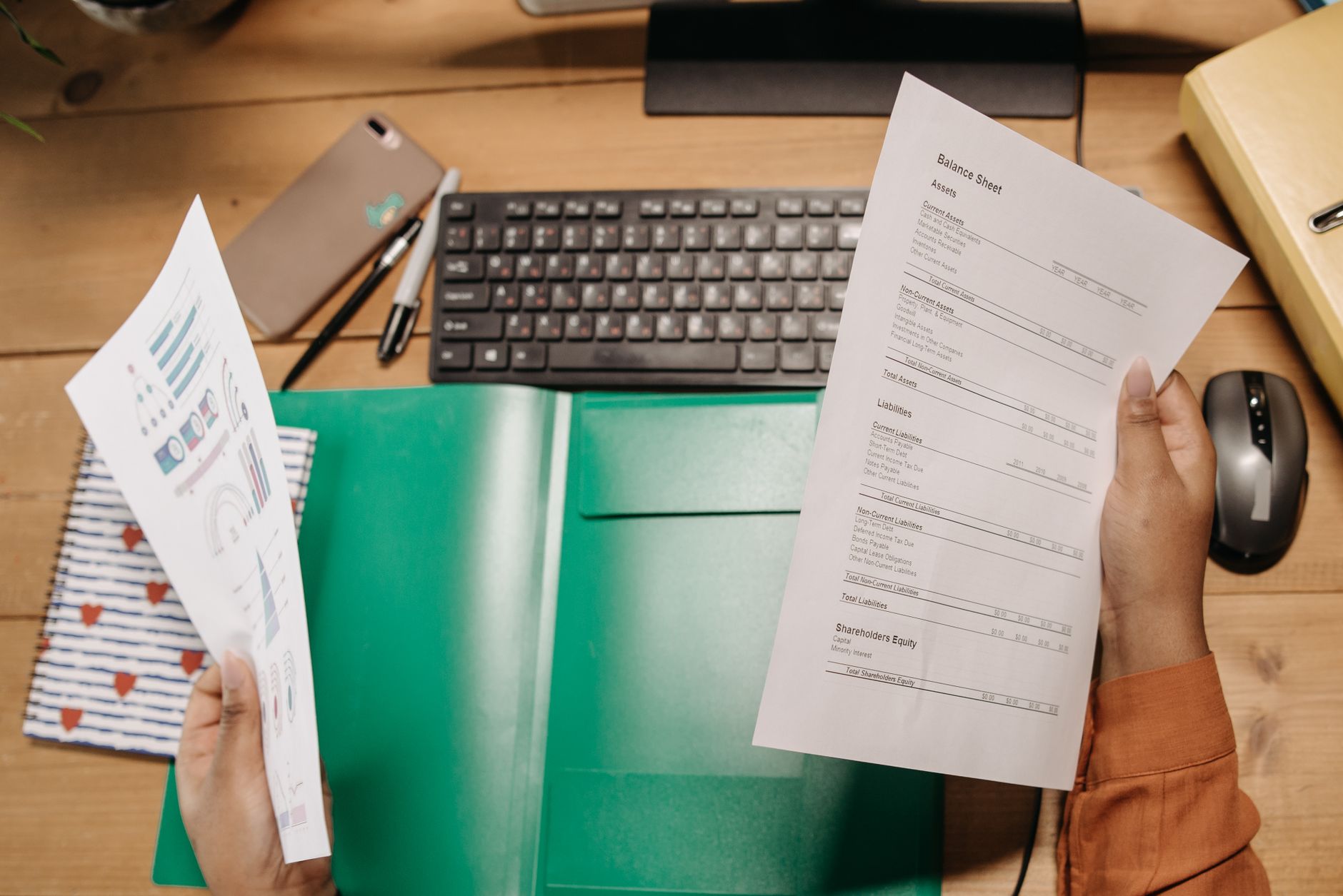 Hands holding and reviewing balance sheets over a desk with a keyboard and stationery — UPI Study