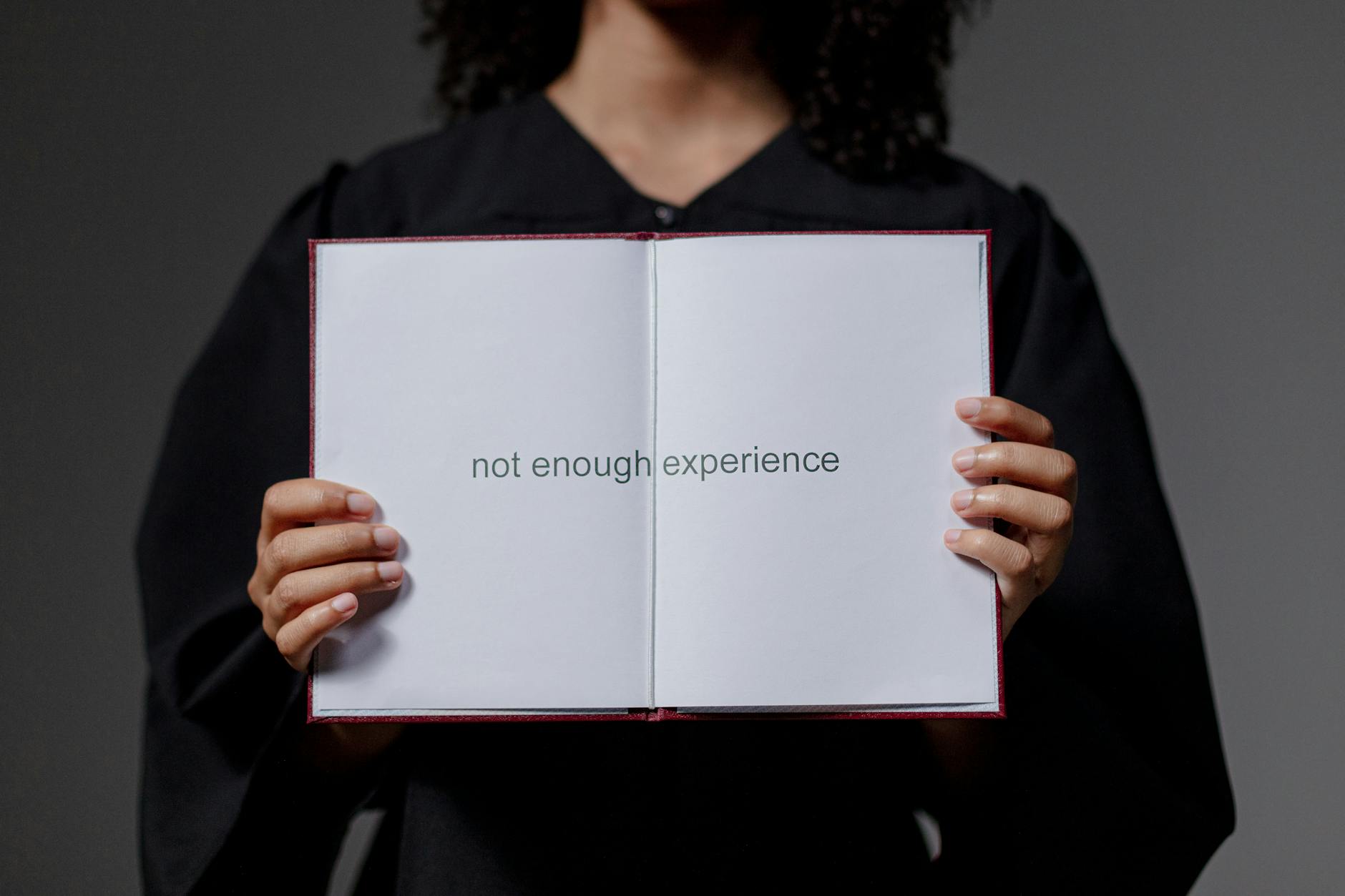A graduate in cap and gown displays a diploma reading 'not enough experience', highlighting job market challenges — UPI Study