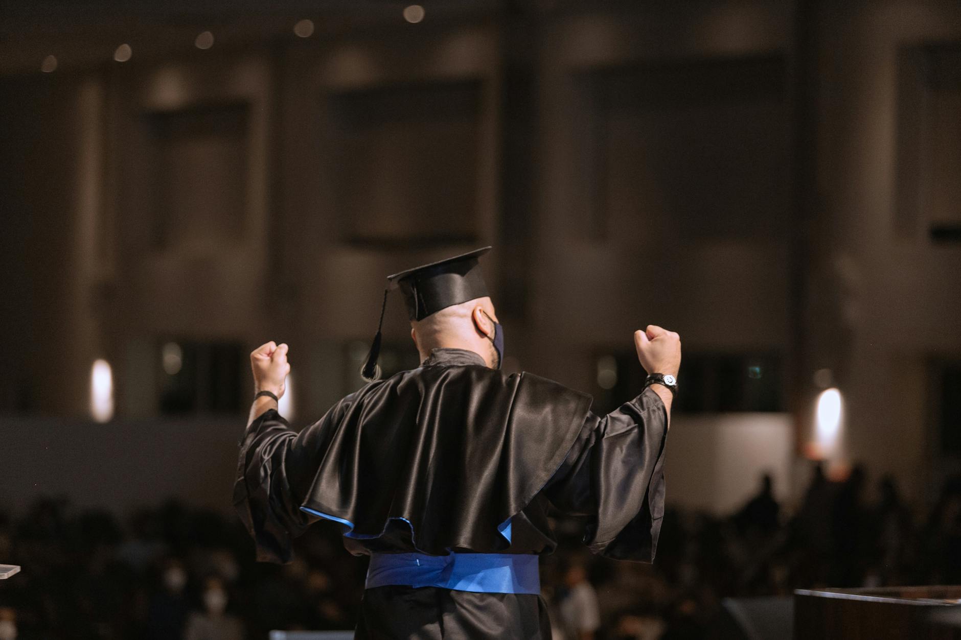 Graduate celebrating success at ceremony with arms raised in joy — UPI Study