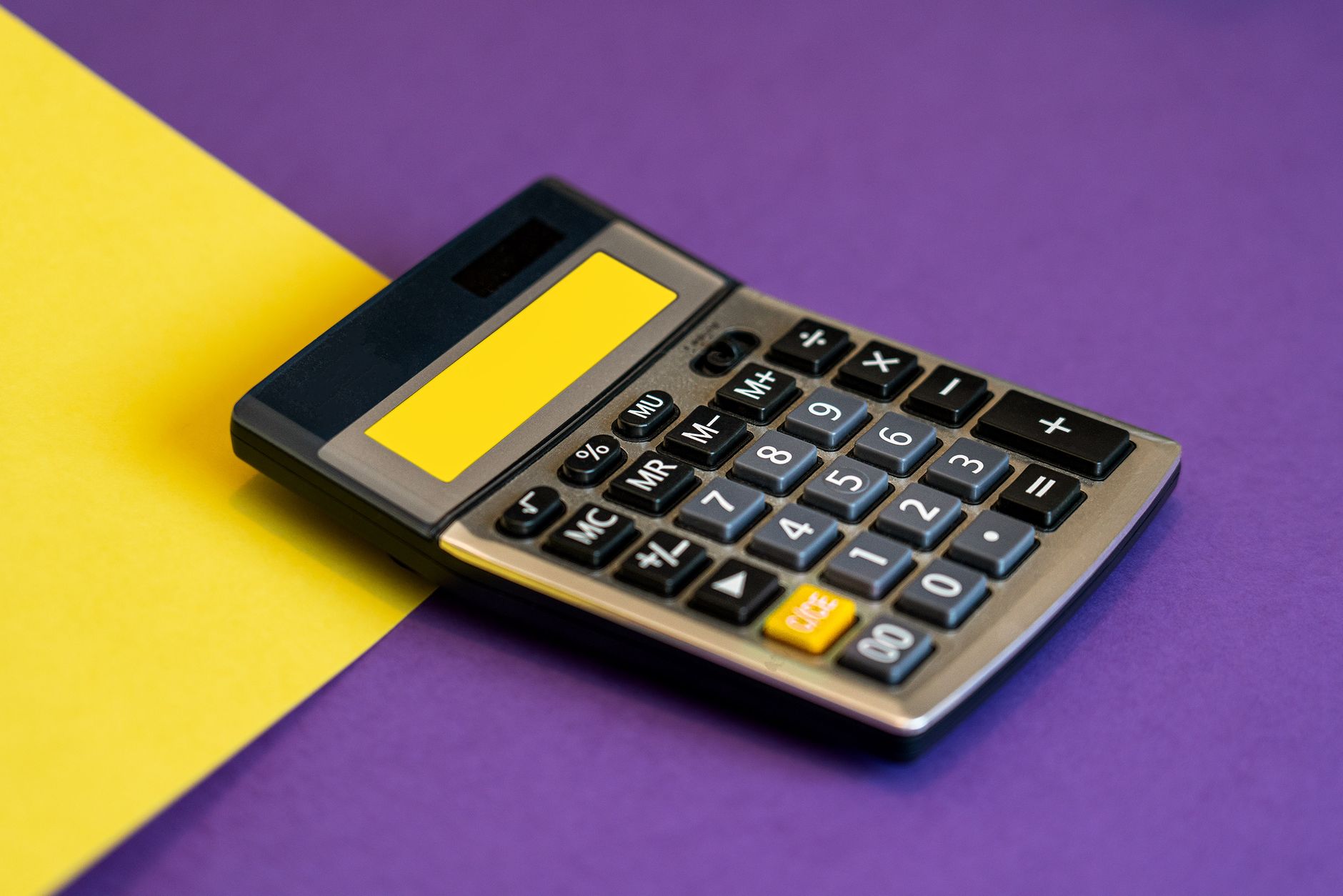 A calculator on vibrant yellow and purple background representing business finance — UPI Study