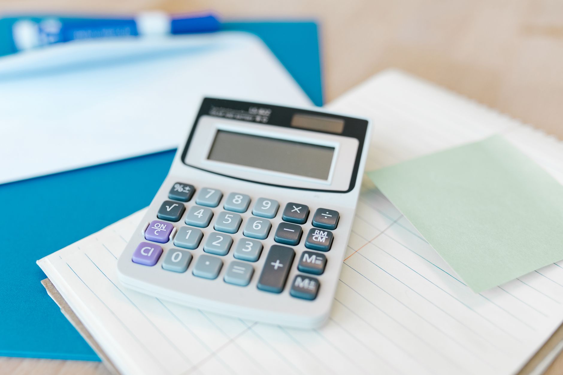 A white calculator on a stack of lined paper with a blue folder, capturing an office setting — UPI Study