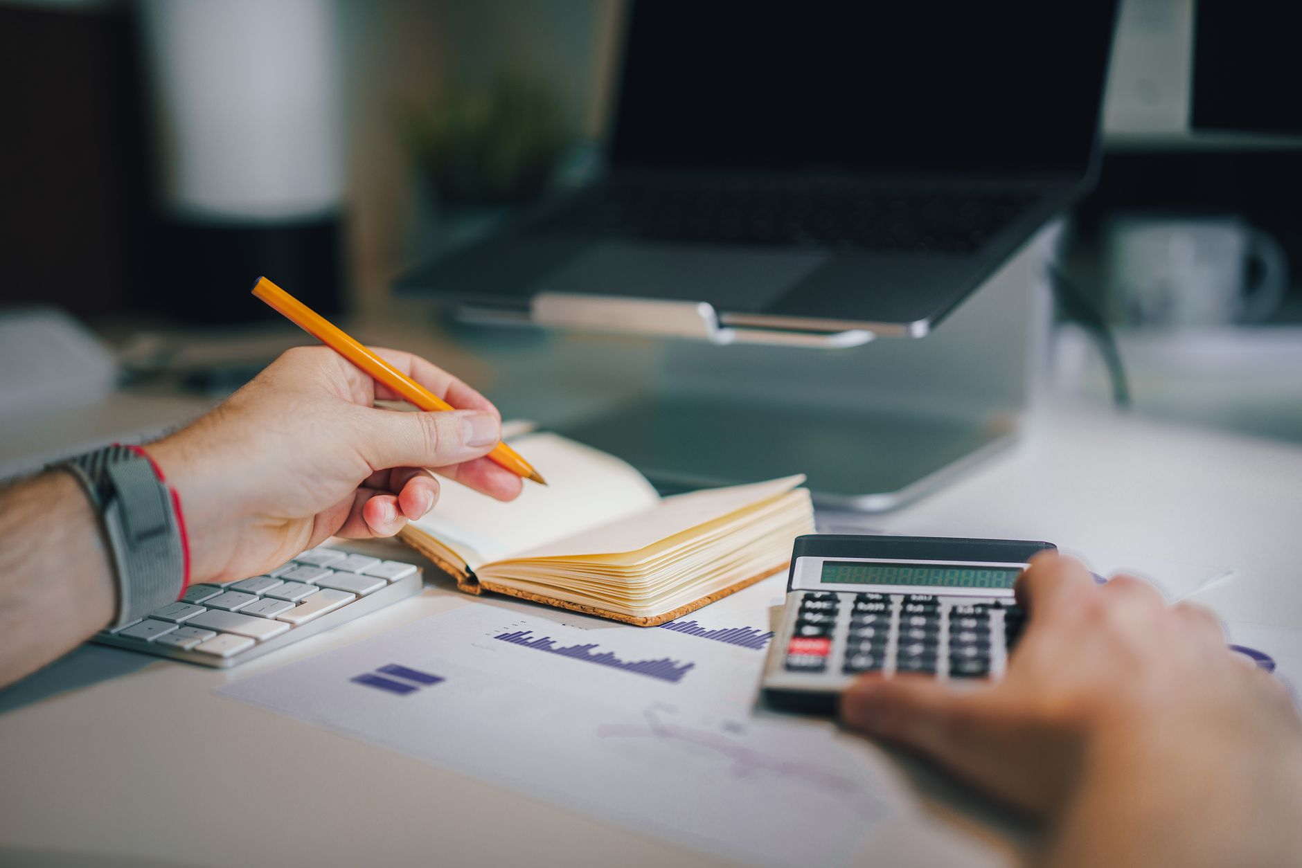 Hands using calculator and taking notes on desk with laptop, showcasing business analytics — UPI Study