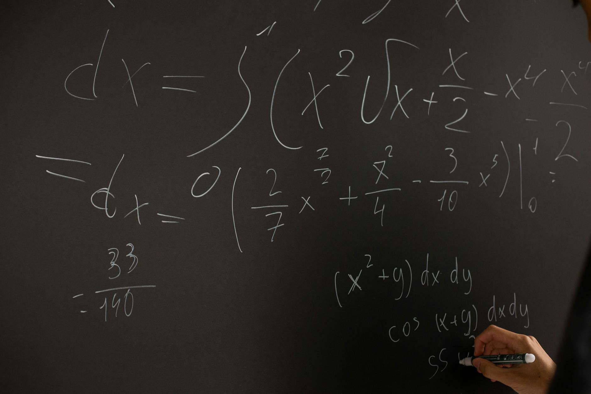 Close-up of hand writing complex math equations on a chalkboard in a classroom setting — UPI Study
