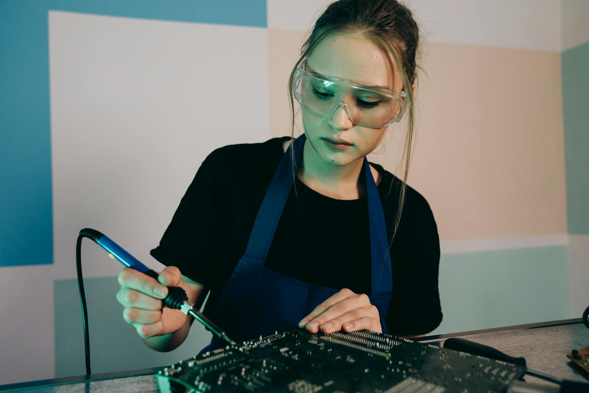 Caucasian woman wearing protective goggles soldering a circuit board, focused on detailed engineering work — UPI Study