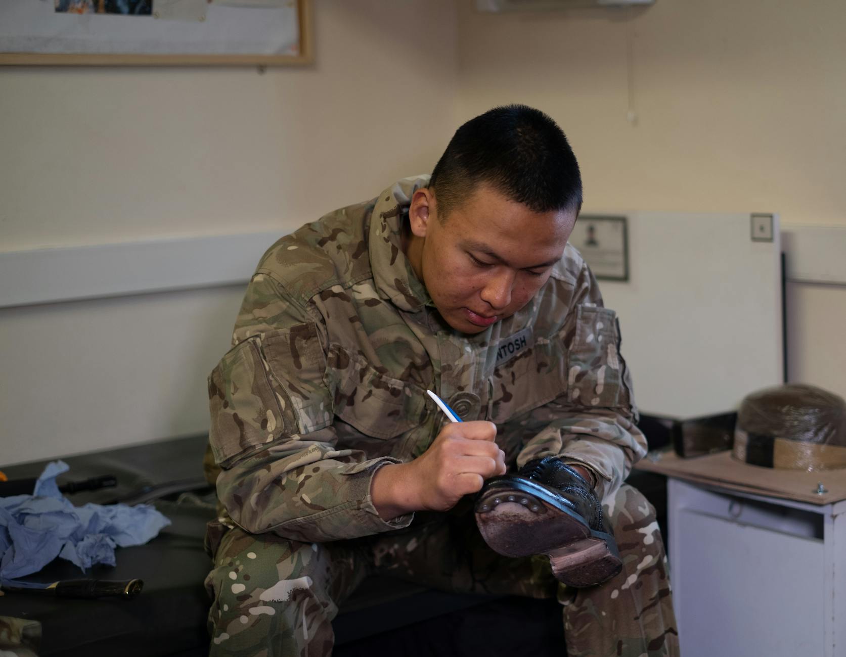 A British soldier is polishing boots indoors, showcasing military routine and discipline — UPI Study