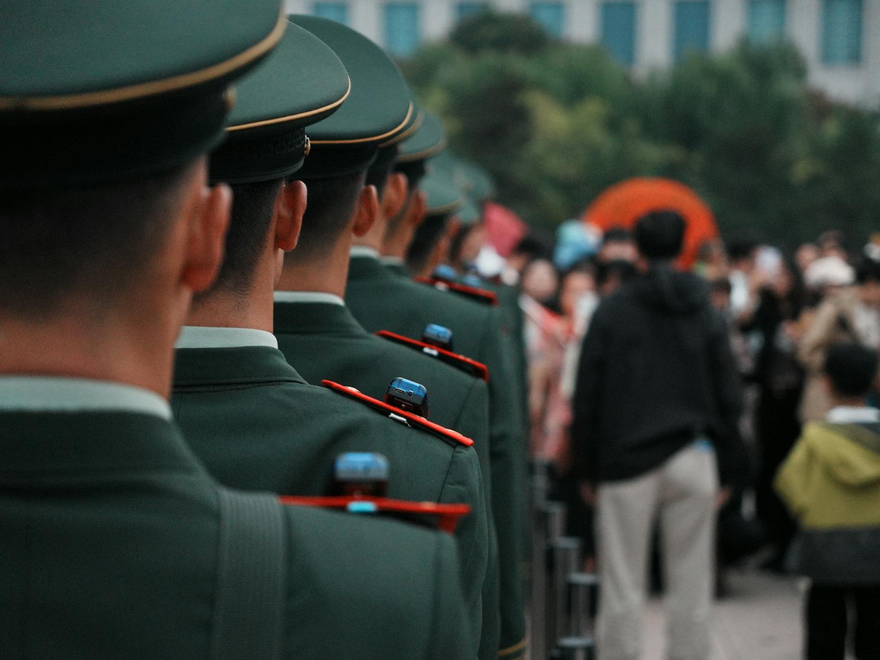 Military officers in green uniforms stand in line formation outdoors, facing a crowd — UPI Study