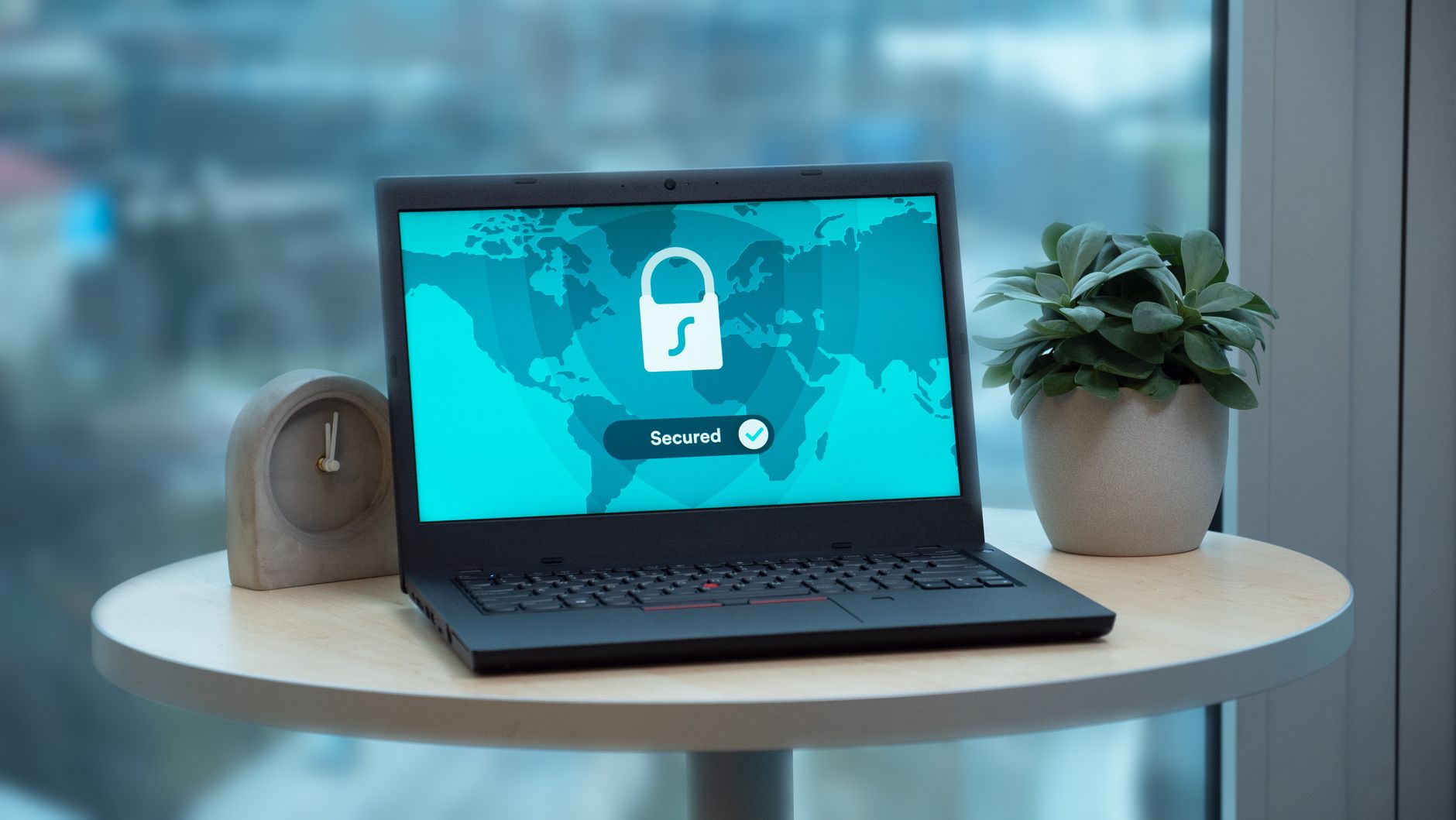 Laptop displaying a security lock icon on a table with a potted plant and clock — UPI Study